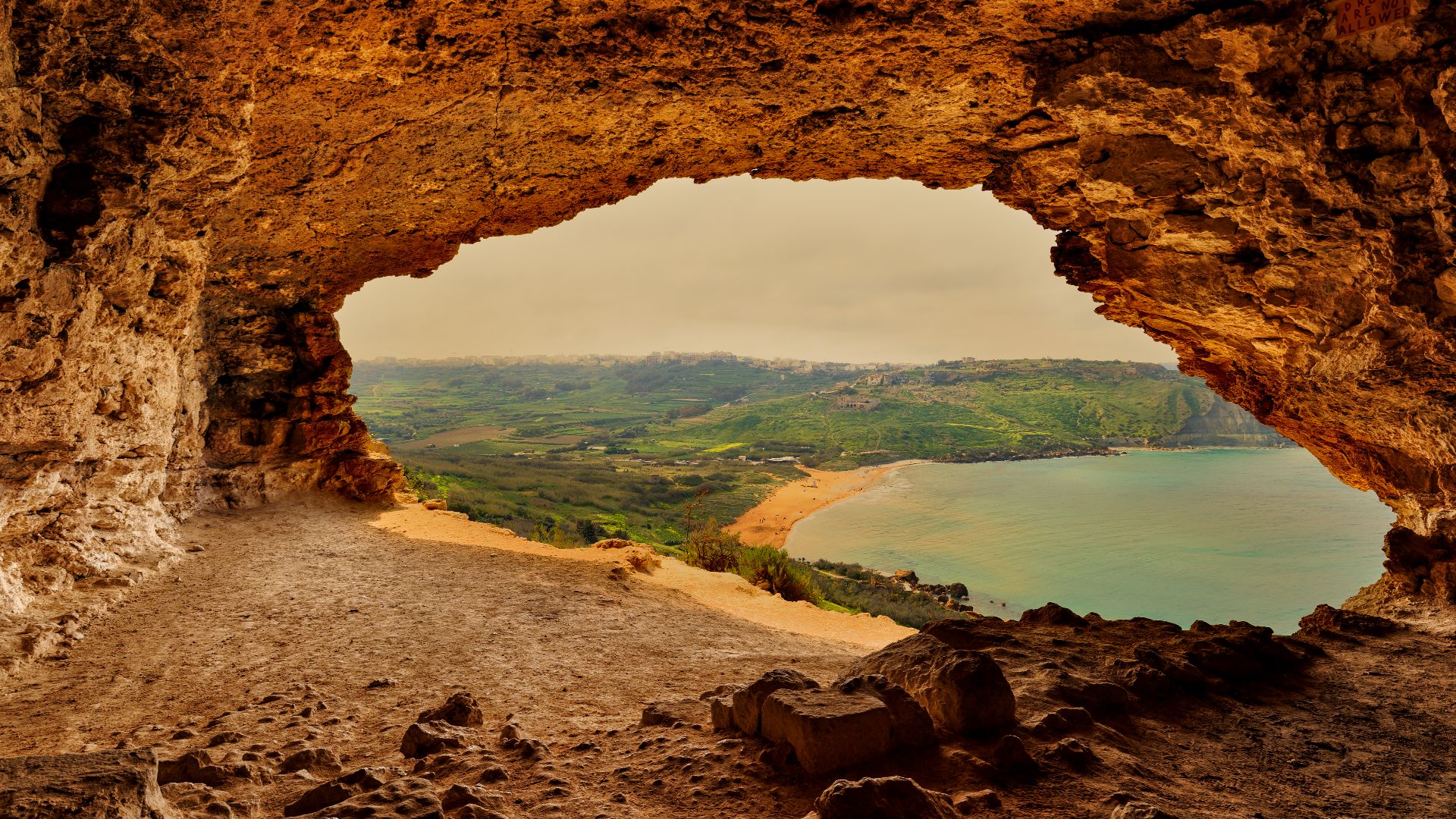 This view from Tal-Mixta Cave overlooks the iconic red sands of Ramla Bay in Gozo, Malta. The cave is situated on the eastern side of the bay, providing a popular scenic viewpoint.
The cave is a popular tourist attraction known for its dramatic natural te