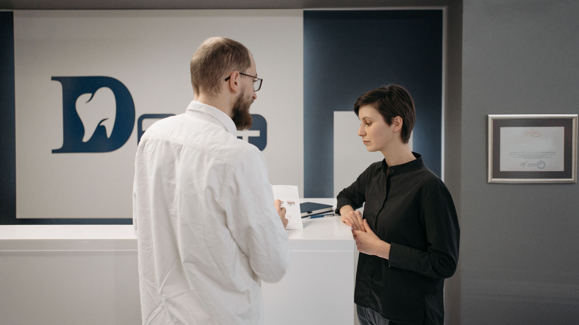 A male dentist consulting a female patient at a modern dental clinic reception.