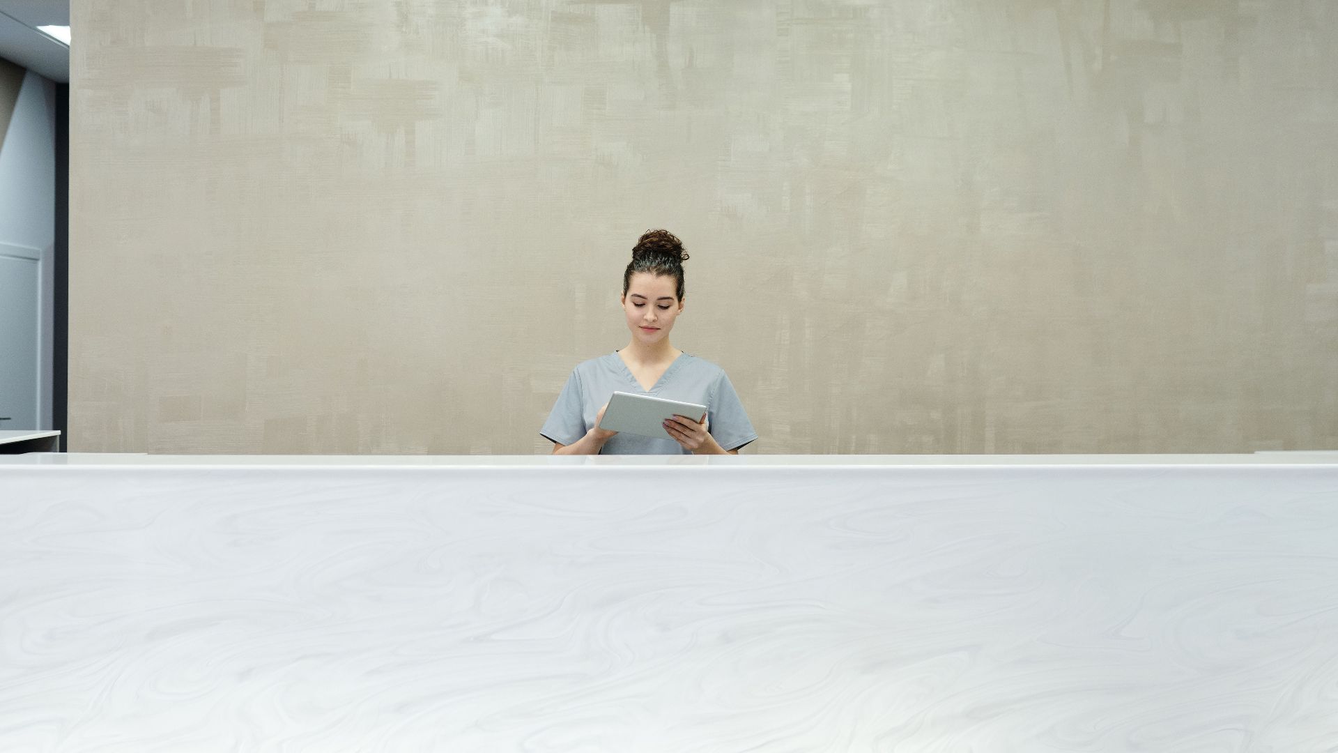 A woman receptionist using a tablet at a modern office reception desk.