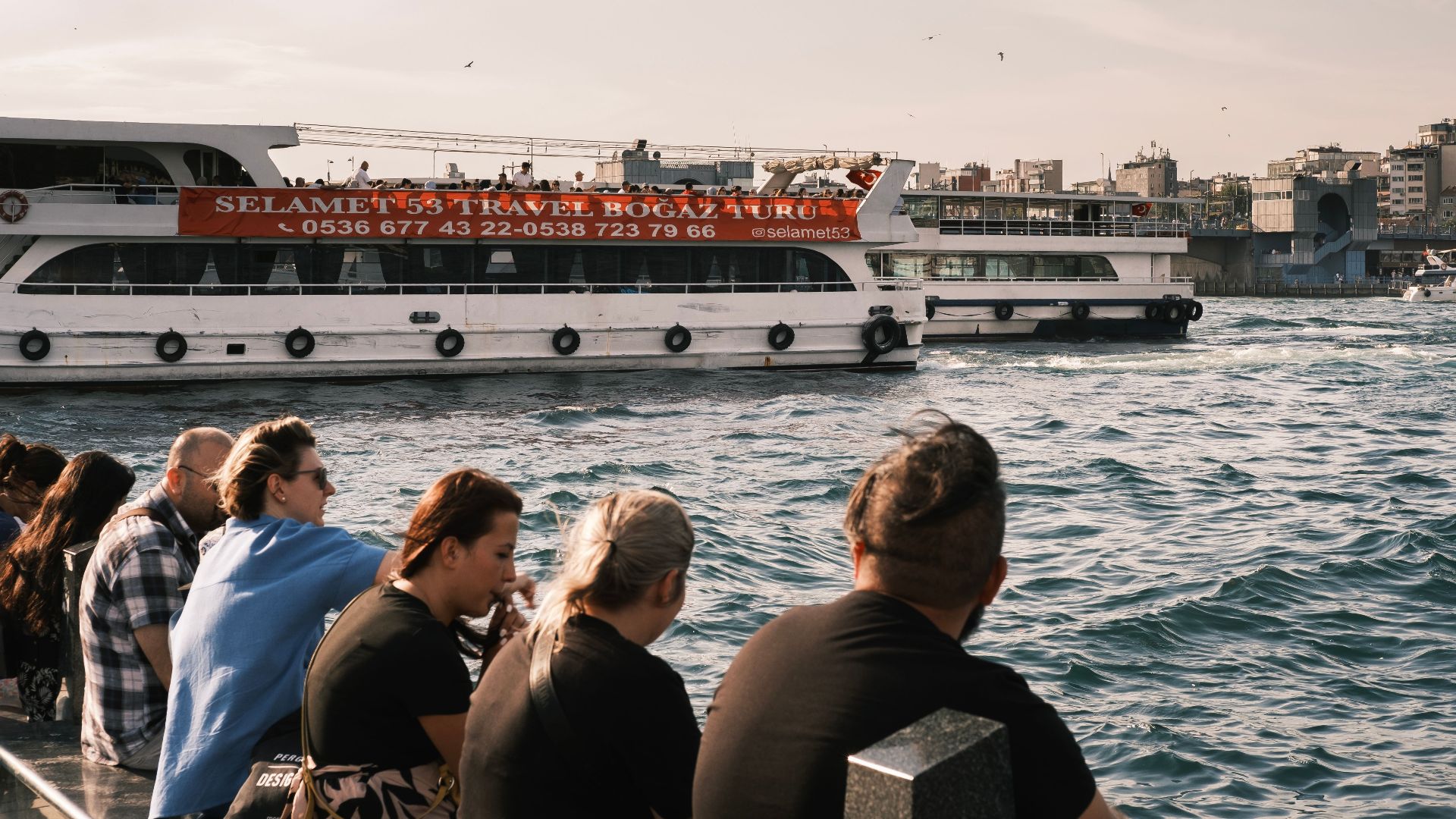 Ferry cruising on Istanbul waters with tourists and cityscape backdrop.