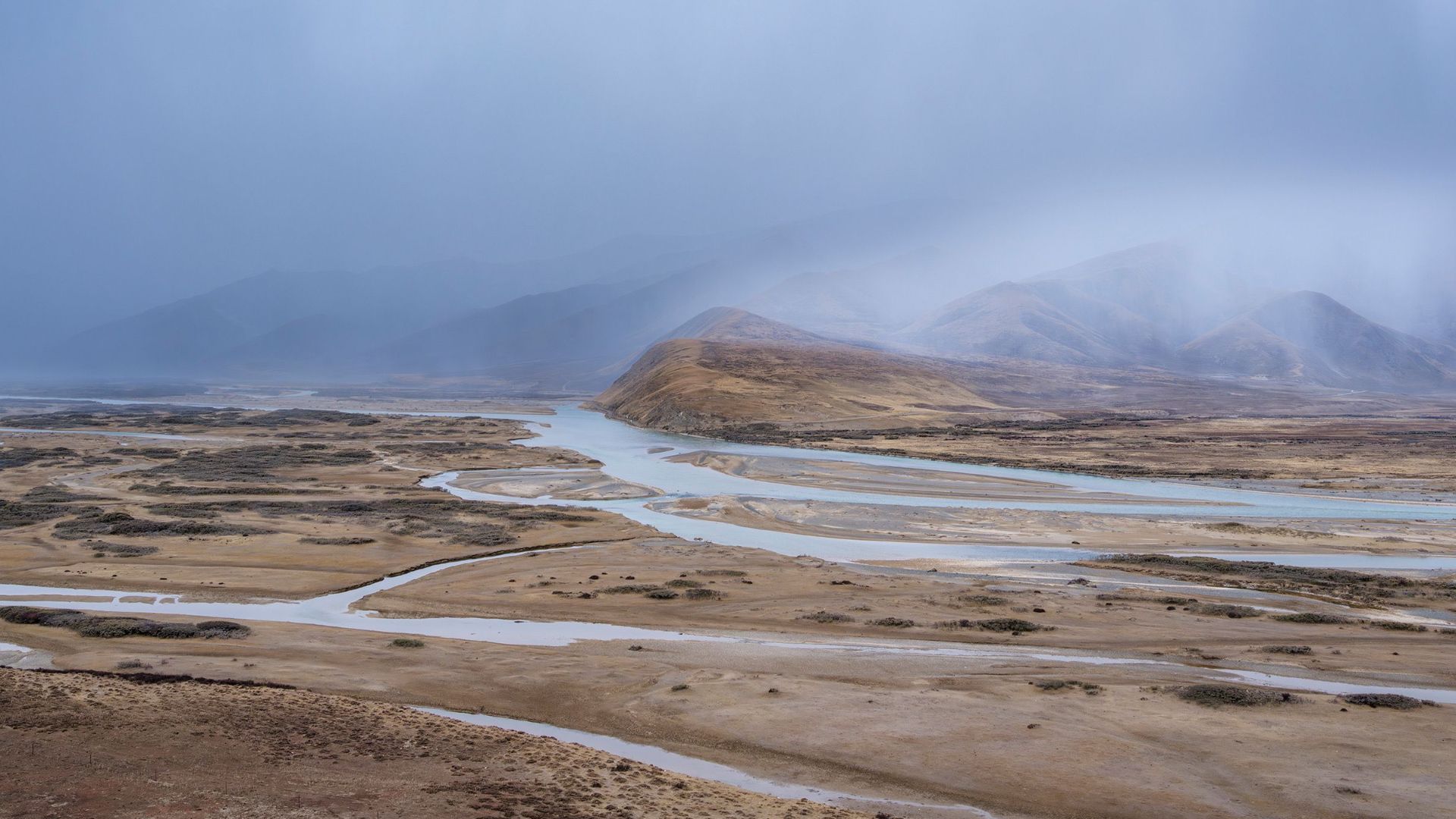 Moody landscape of a desert valley with rainfall and winding river