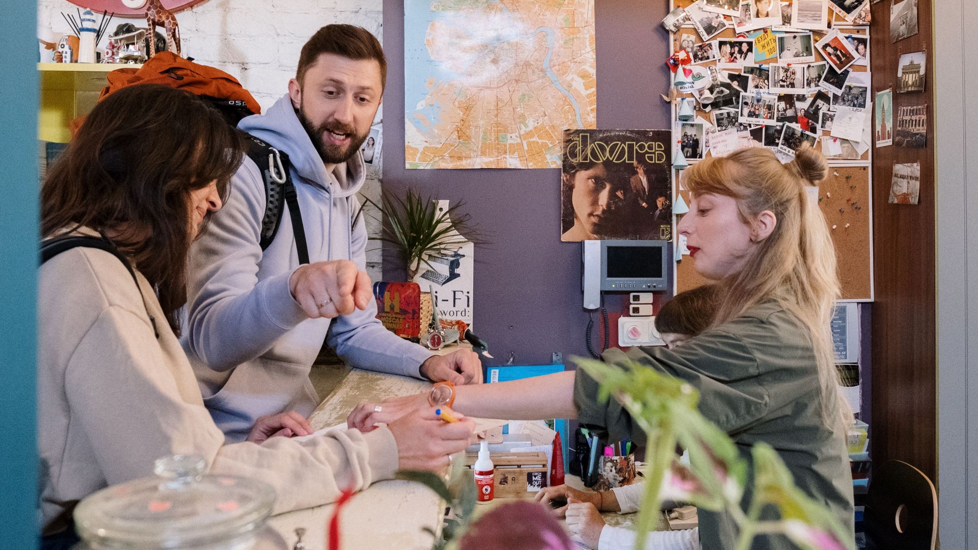 Guests checking in at a hostel reception with a warm interaction between a couple and staff.