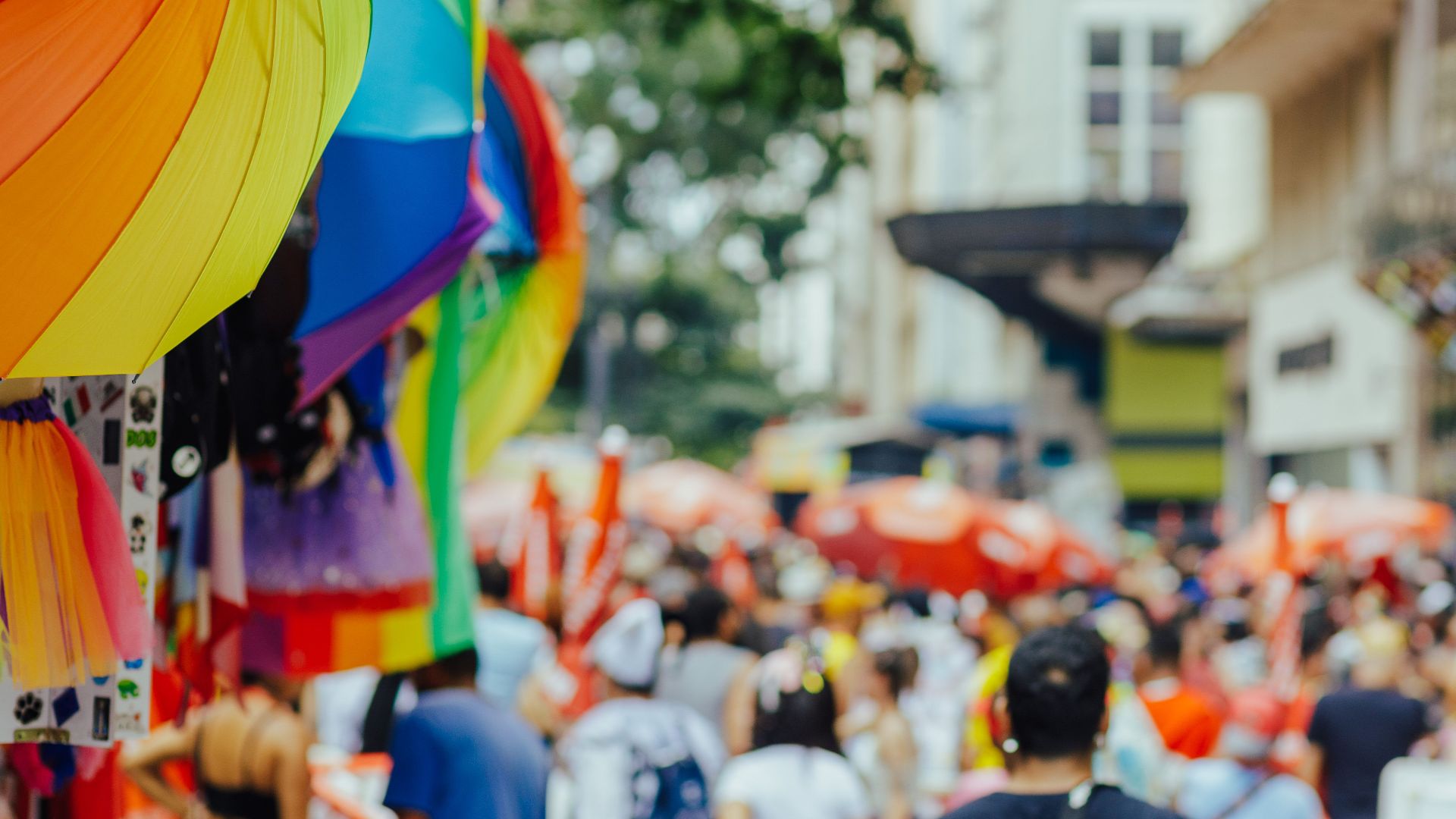 Colorful rainbow umbrellas adorn a lively outdoor city festival with a bustling crowd.