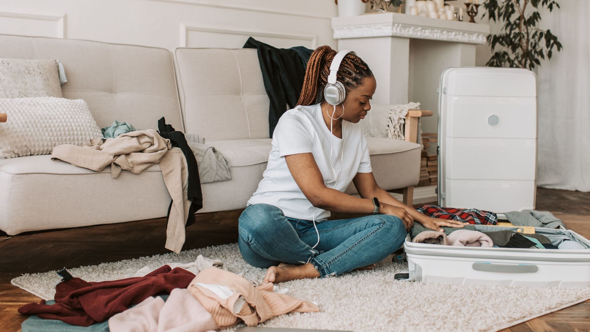 A woman with headphones packing a suitcase in her stylish living room, preparing for travel.