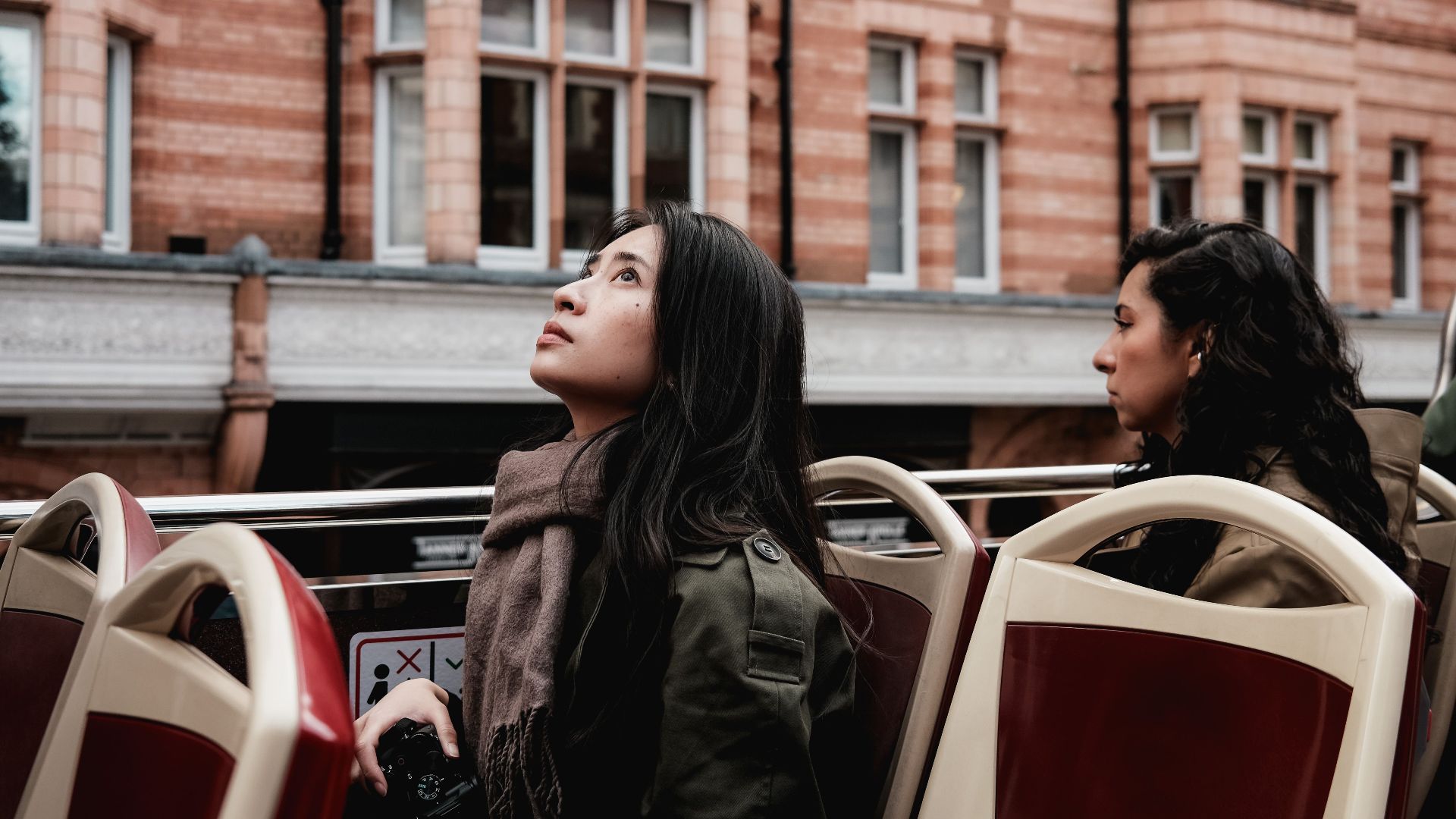 Two women on an open-top bus admire historic architecture in an urban setting.