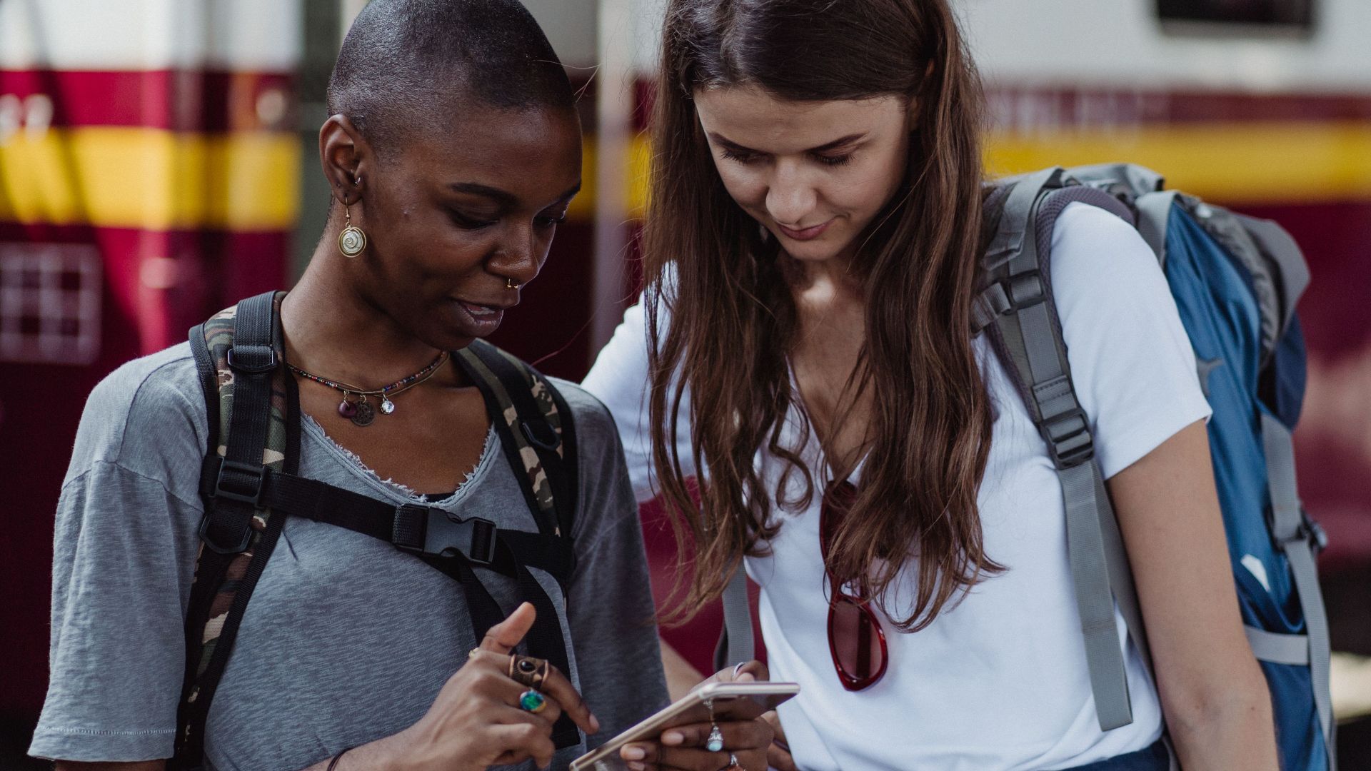 Two female travelers looking at a smartphone while waiting at a train station.