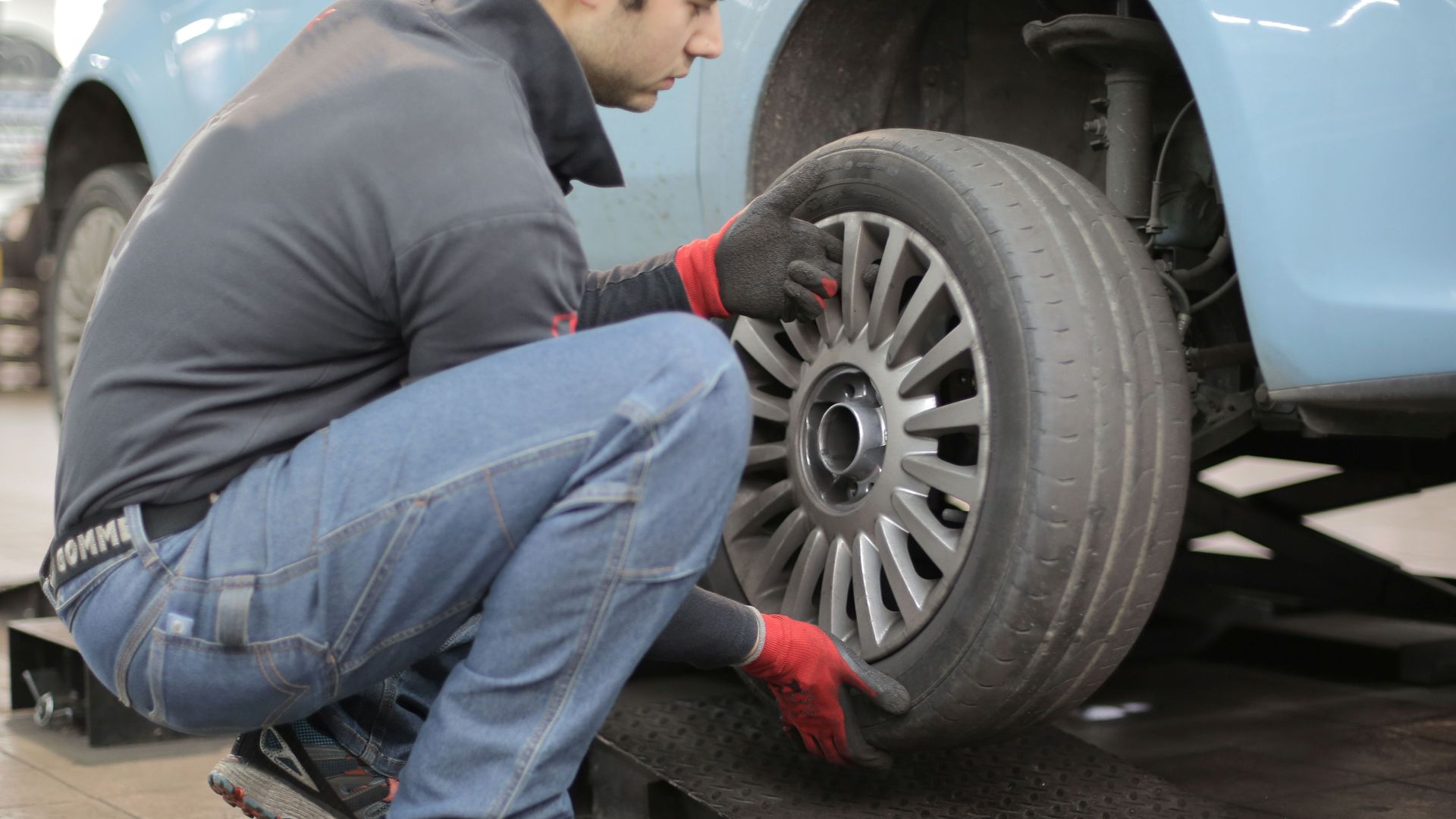 Mechanic changing a car tire indoors, using tools for vehicle maintenance.