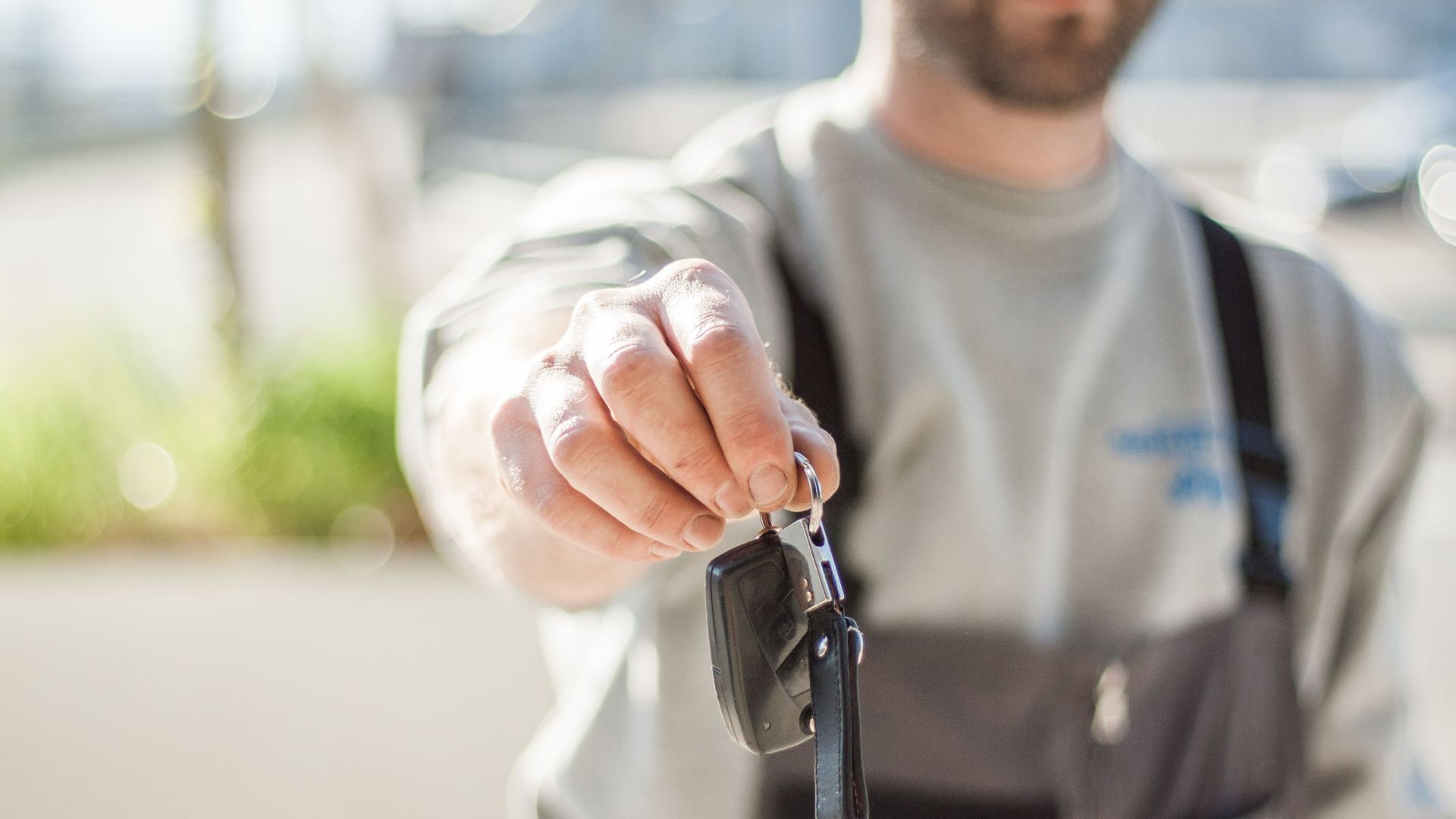 Hand holding a car key outdoors, blurred background, shallow focus.