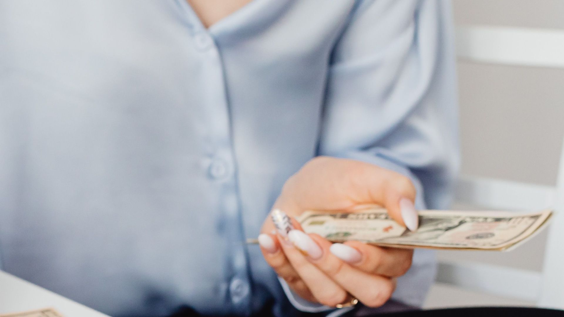A woman counts US dollar bills at a desk, symbolizing finance management.