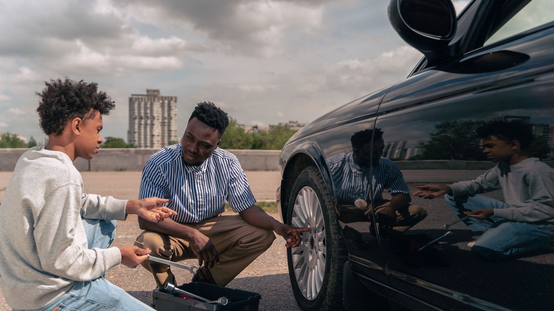 Father and son bonding while learning tire maintenance outdoors. Daytime photo.