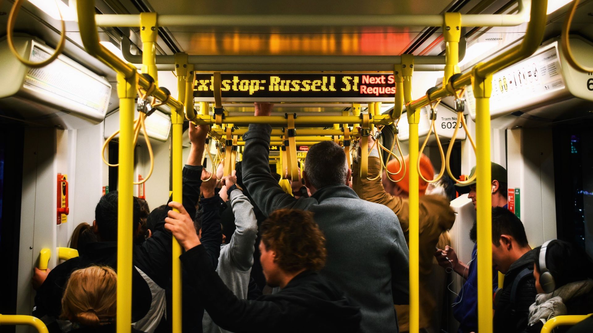 Commuters standing inside a tram in Melbourne with yellow poles and busy atmosphere.