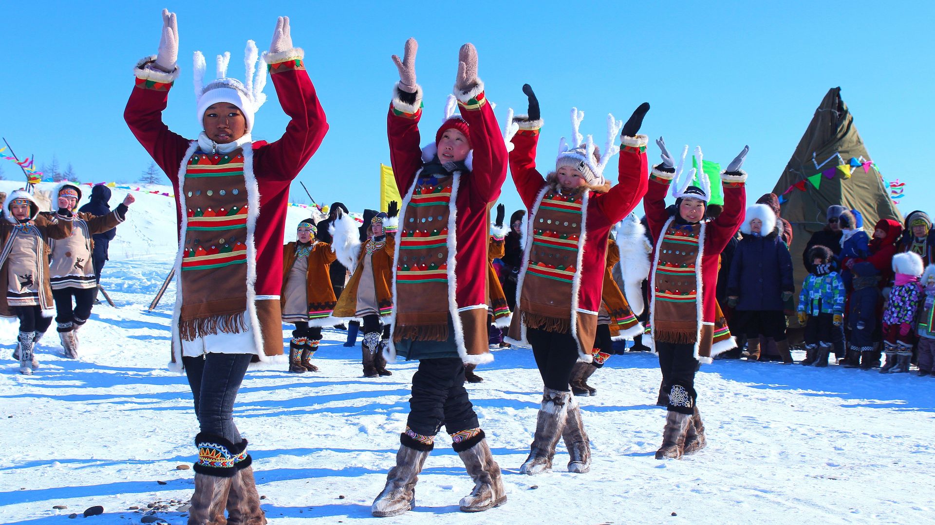 Dancers in traditional attire perform in snowy landscape, celebrating winter culture.