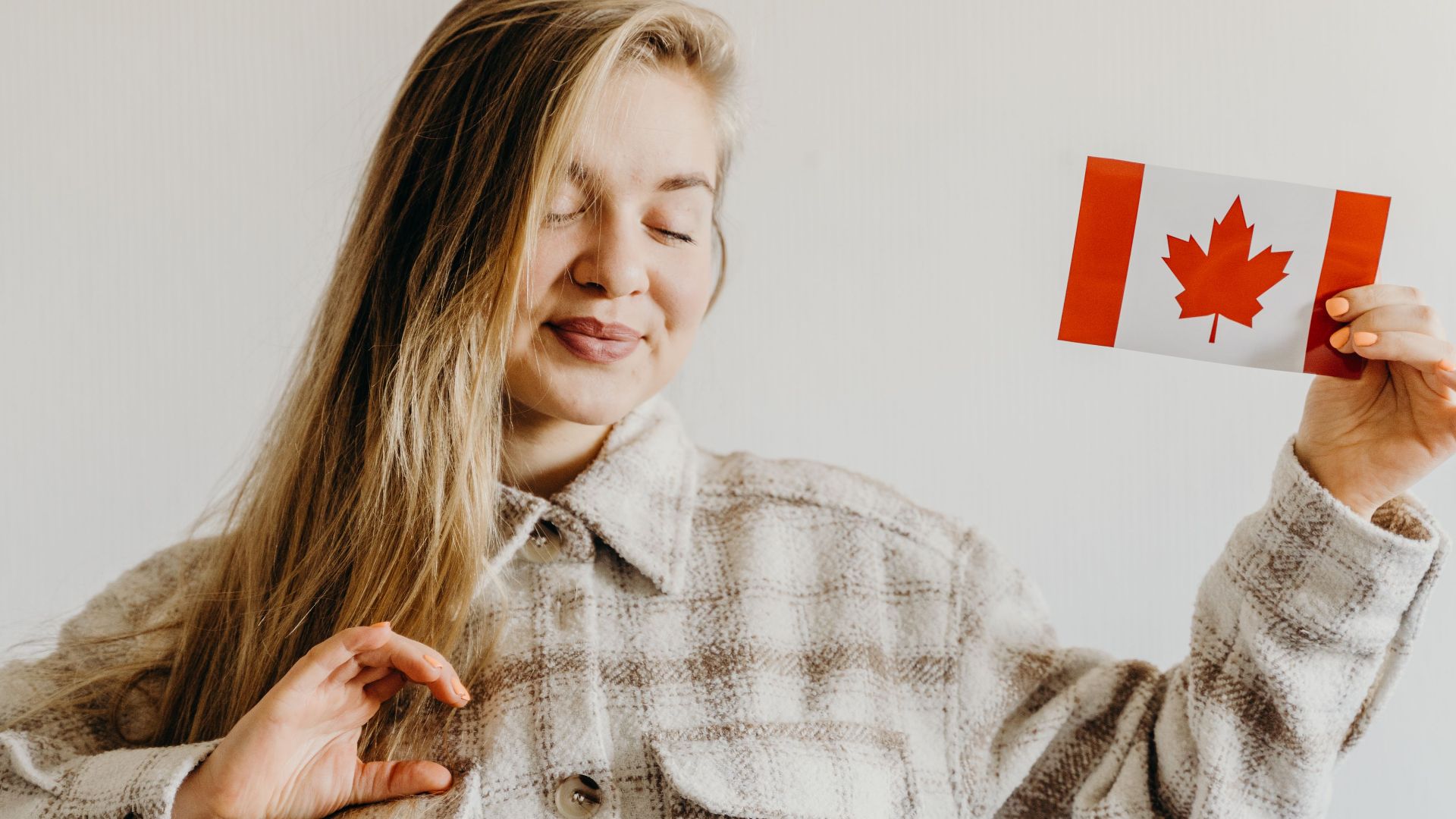 Blonde woman with closed eyes holding Canada flag symbolizing pride and celebration.