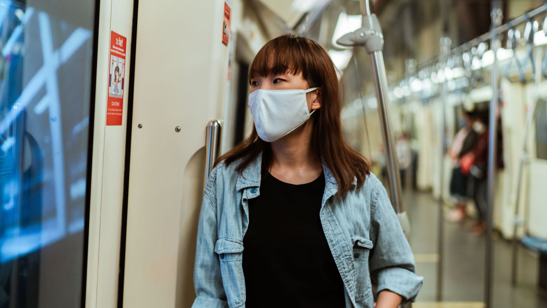 Asian woman wearing a face mask while standing inside a subway train, practicing safety during pandemic.