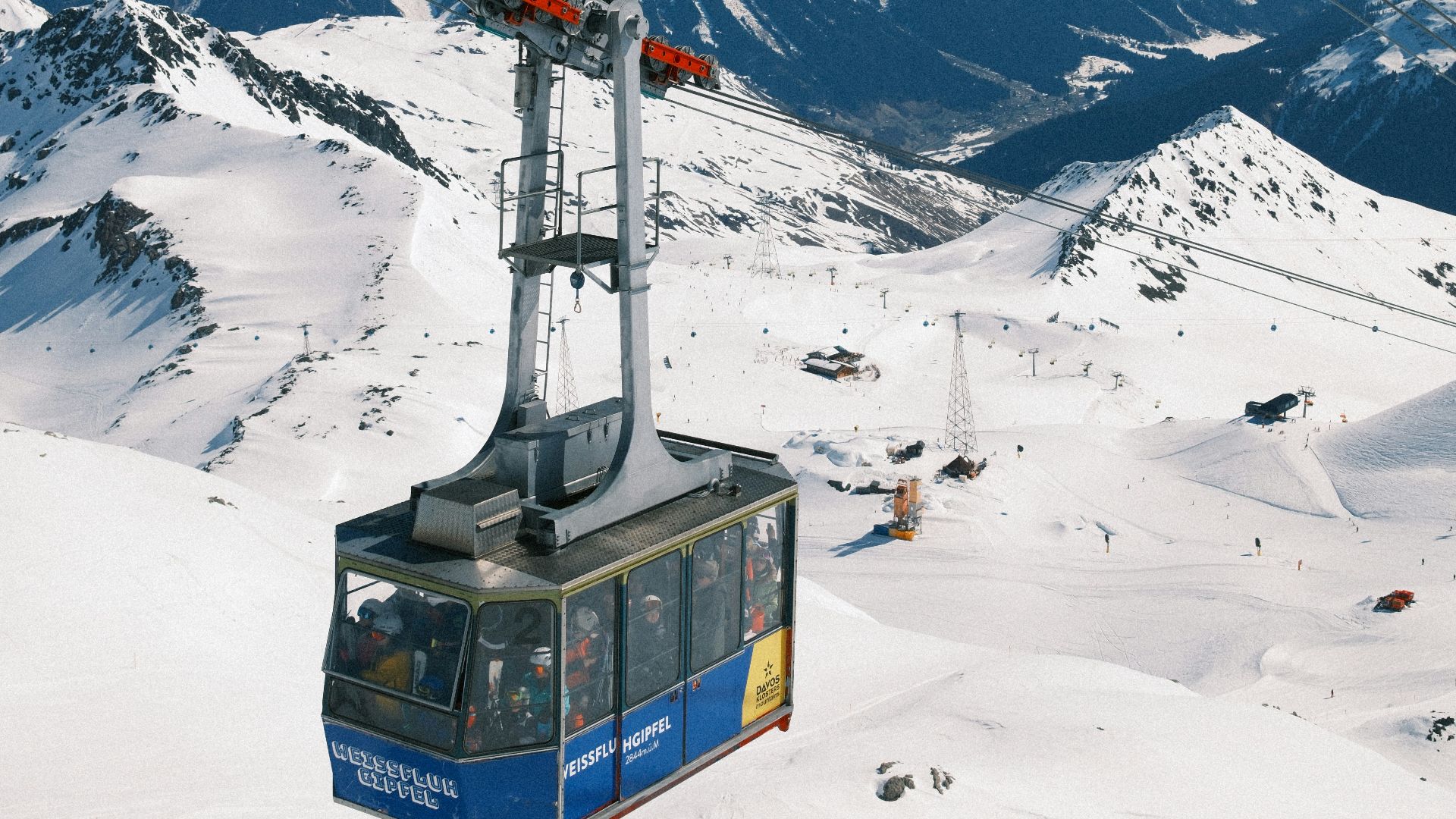 Cable car ascending snowy mountain range under blue sky