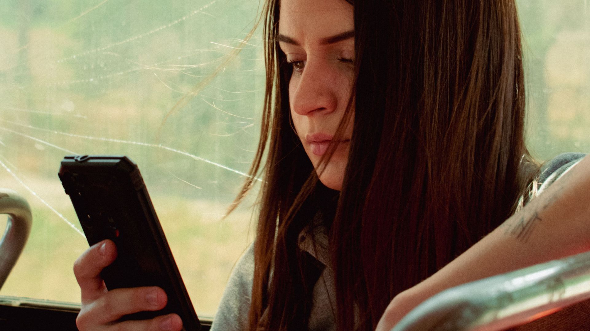 A young woman engrossed in her phone while traveling on a bus during the day.