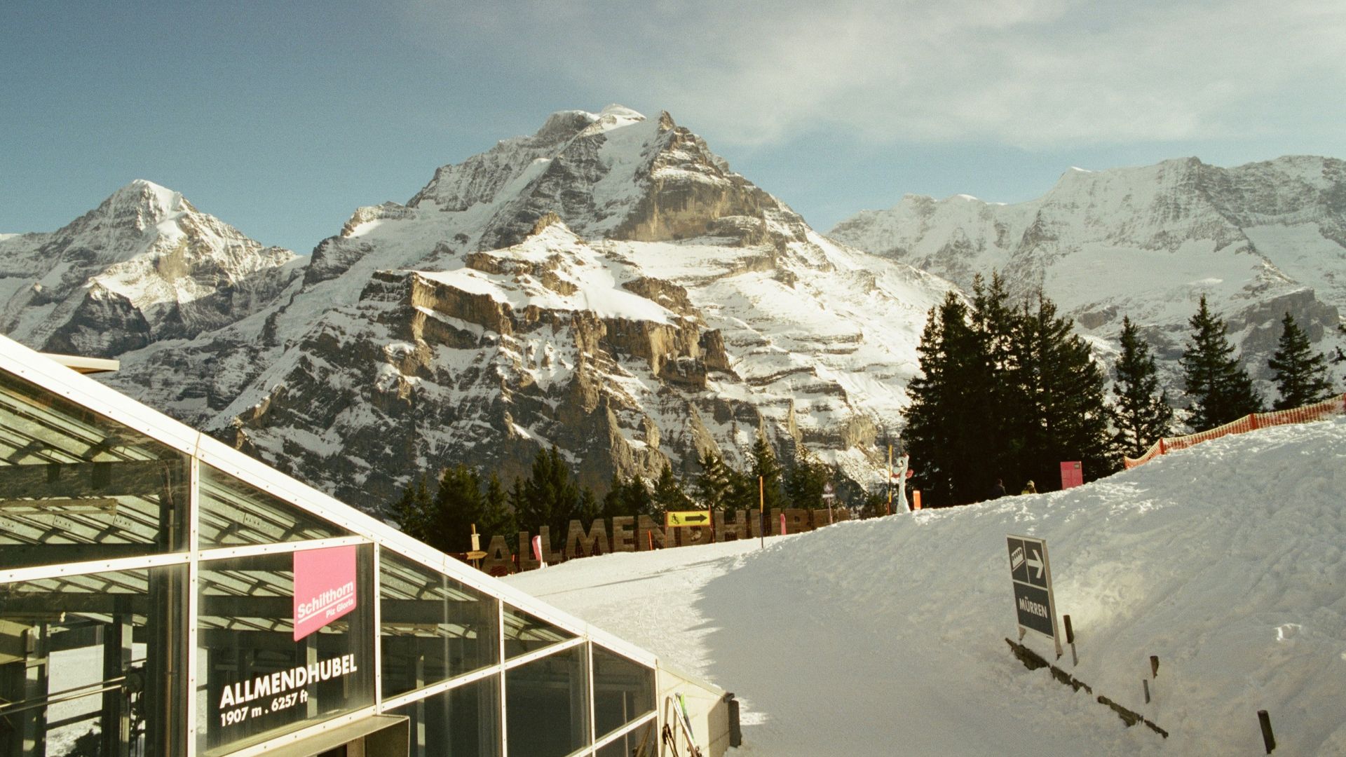 Glass building next to a snowy path with towering mountains