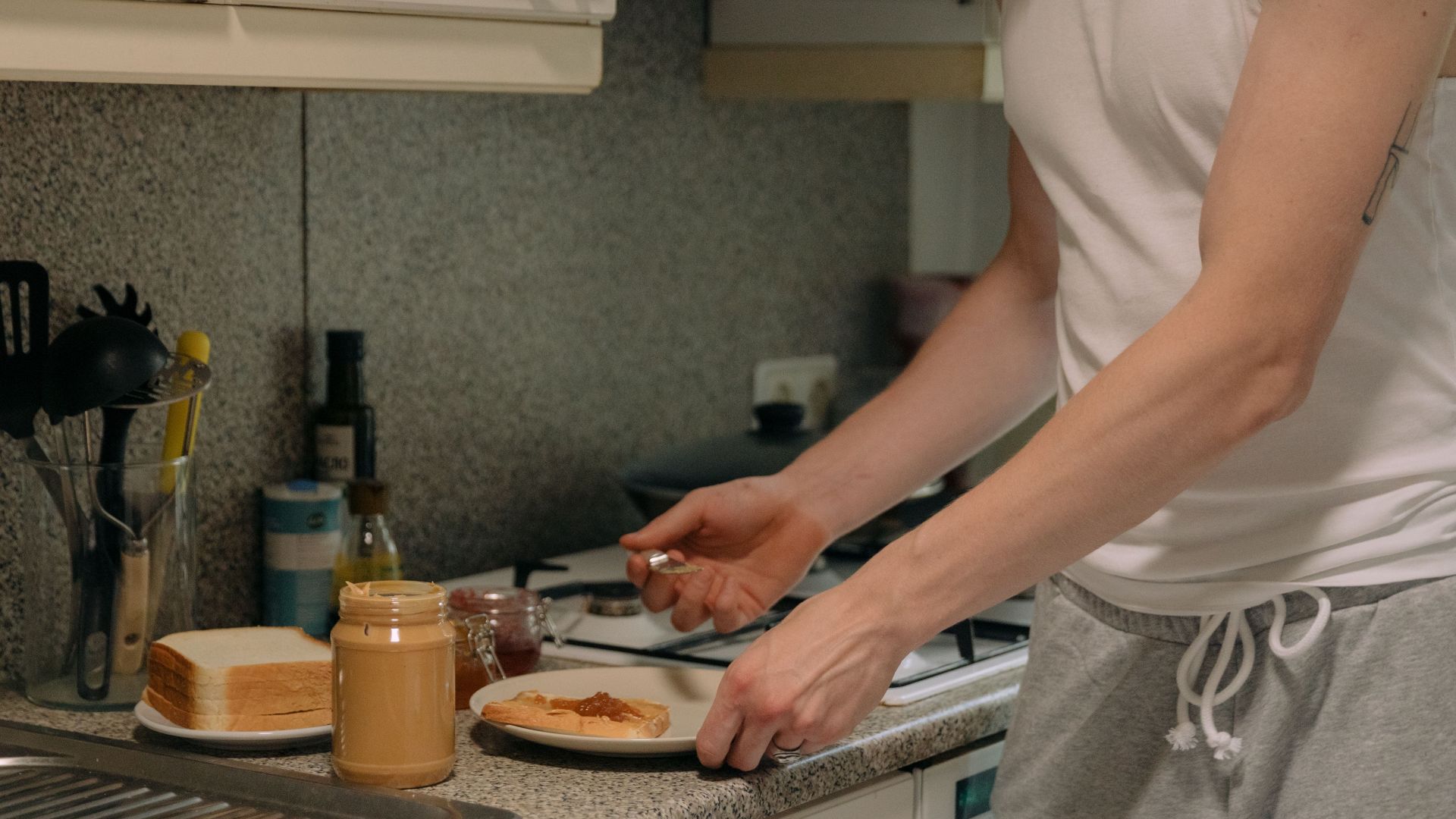 A person prepares a classic peanut butter and jelly sandwich on a kitchen counter.