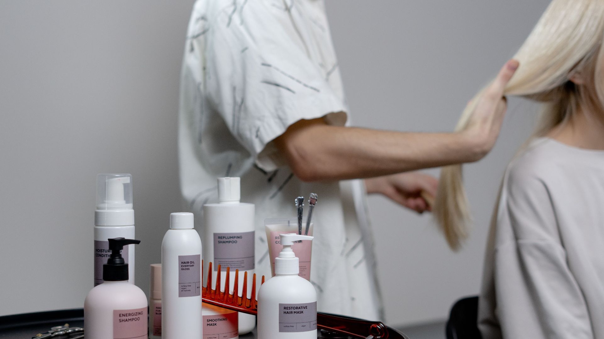 A hairdresser styling a blonde woman's hair in a salon, showcasing hair care products on a table.