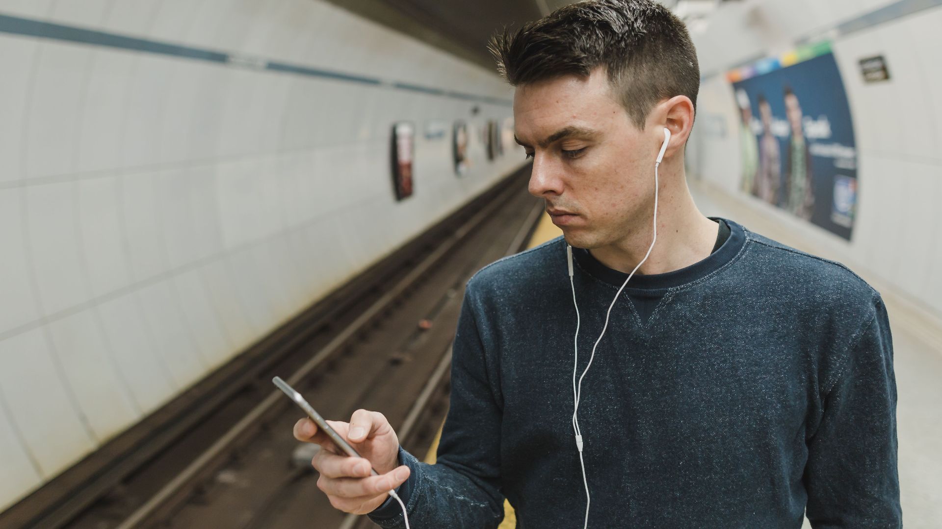 Young man with earphones at subway station using smartphone.