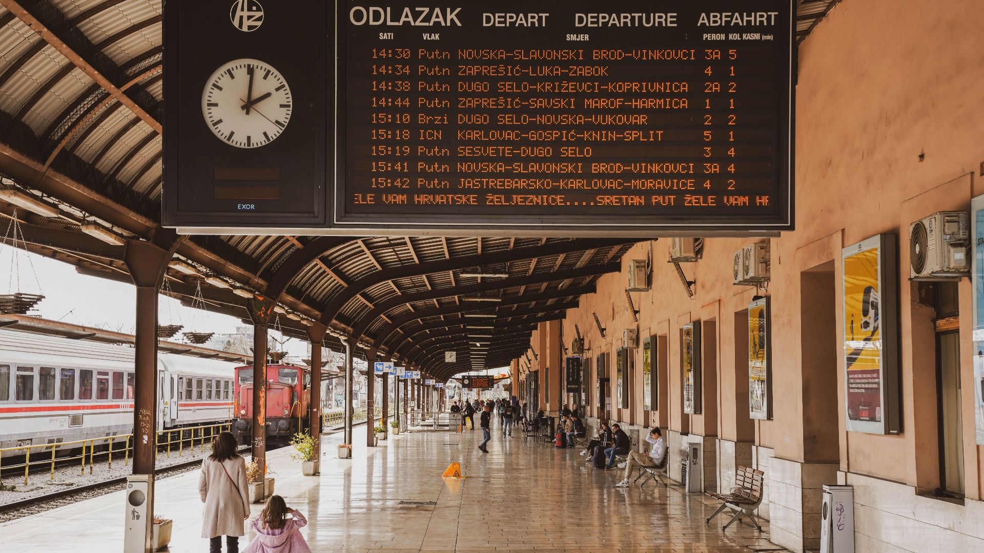 Busy train station in Zagreb with passengers and a large timetable display.