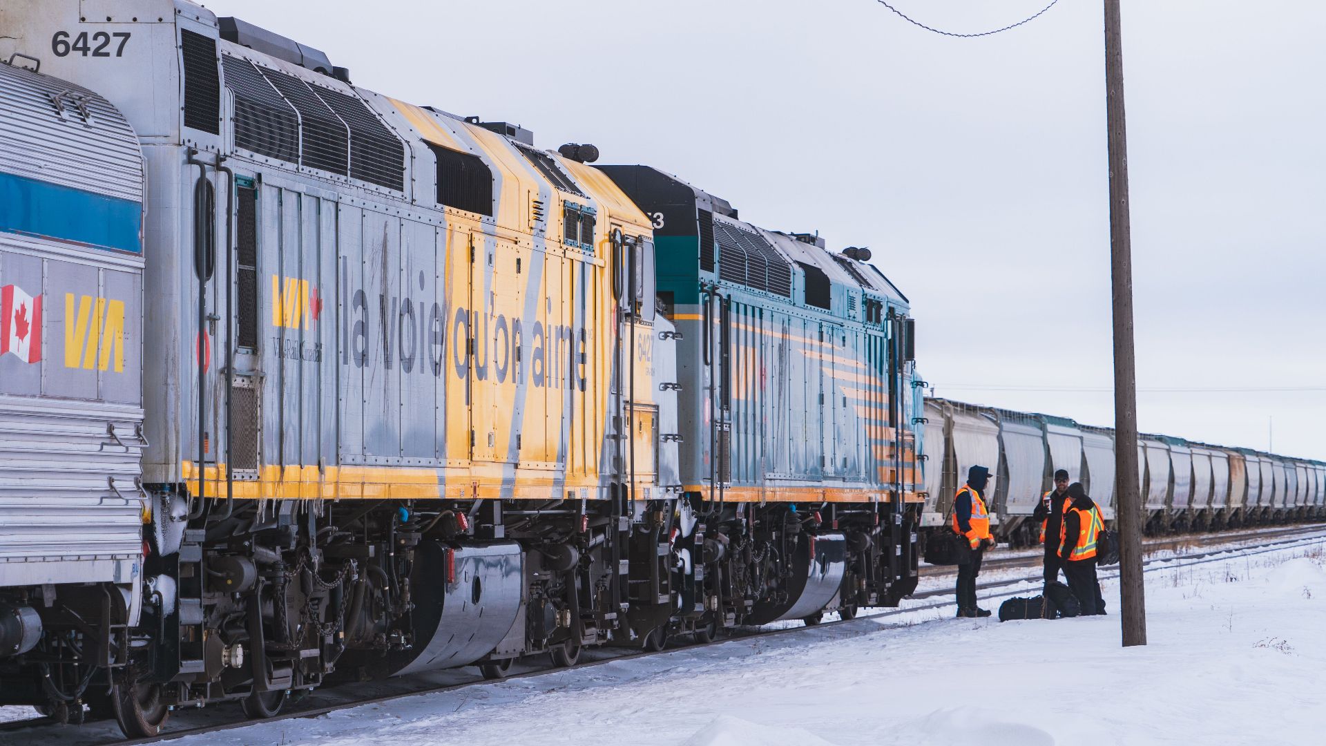 VIA Rail train crossing a snowy field in Canada during winter with railway workers.