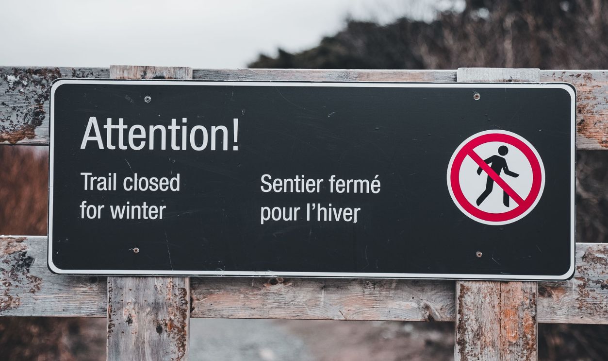 Trail closure warning sign in forest during winter season, landscape view.