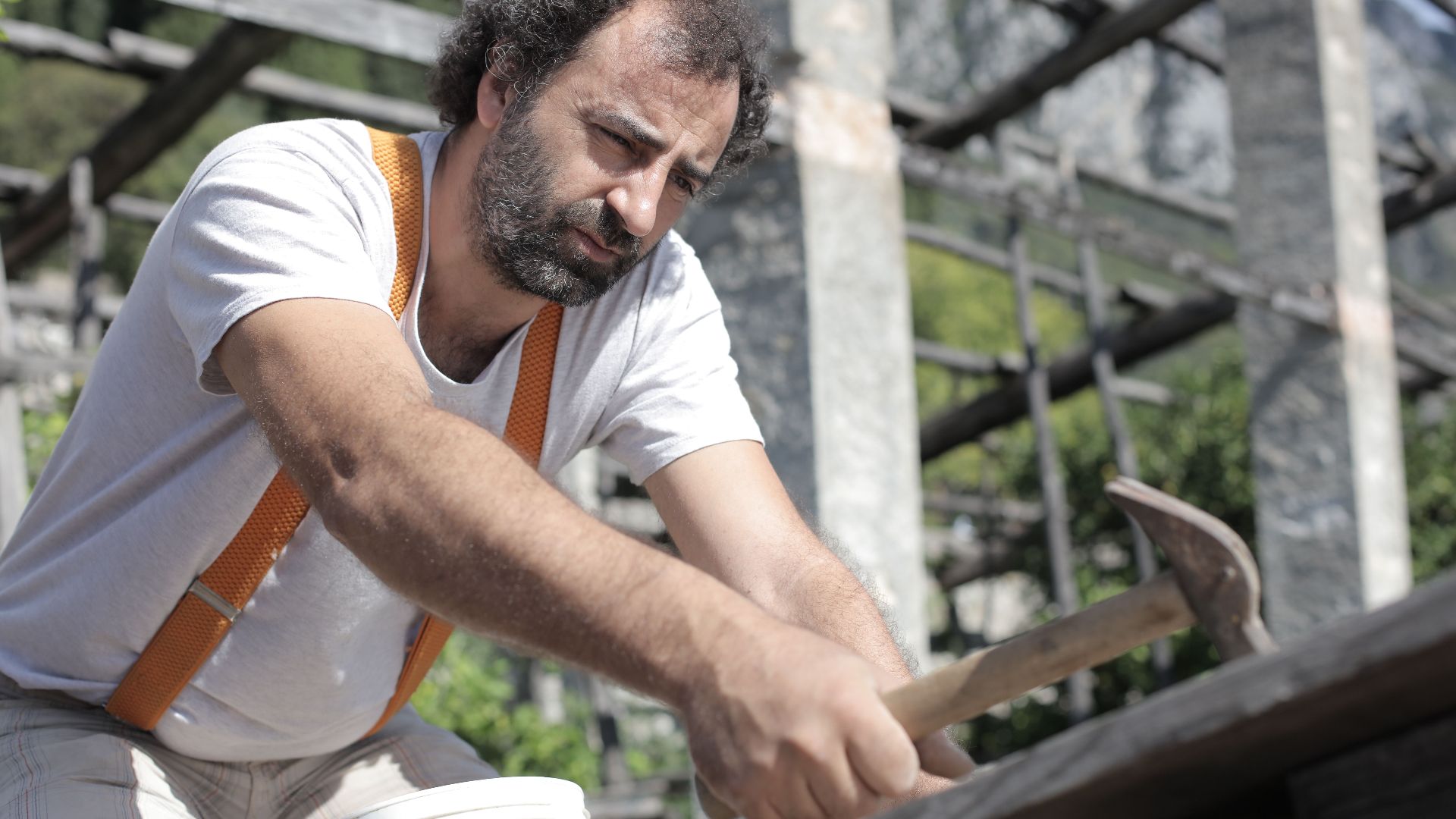 A skilled carpenter attentively uses a hammer during construction work outdoors, showcasing craftsmanship.