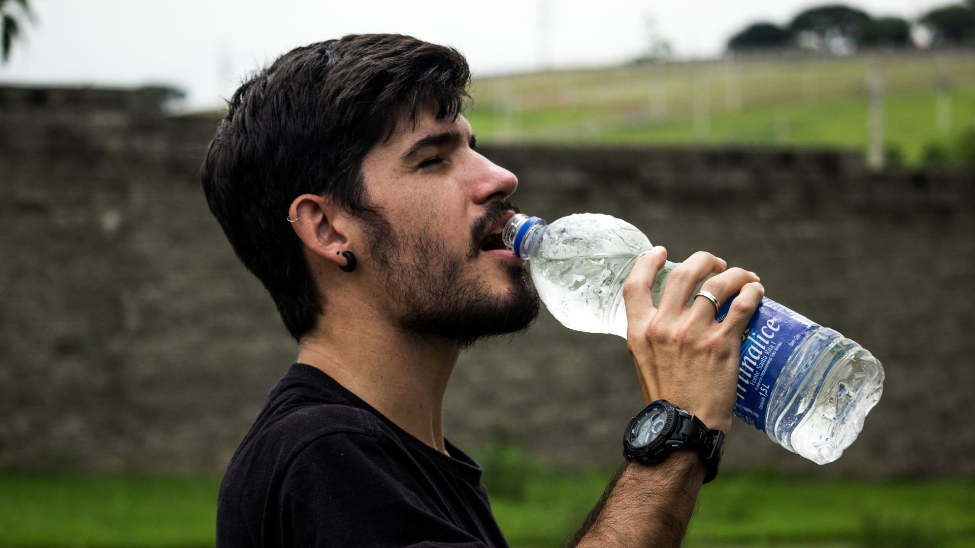 A young man drinks bottled water outside, staying hydrated and refreshed.