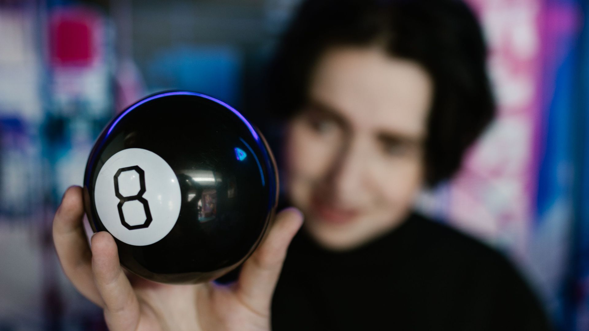 A person holding a magic 8 ball in a dimly lit room with a neon backdrop, creating a mysterious vibe.