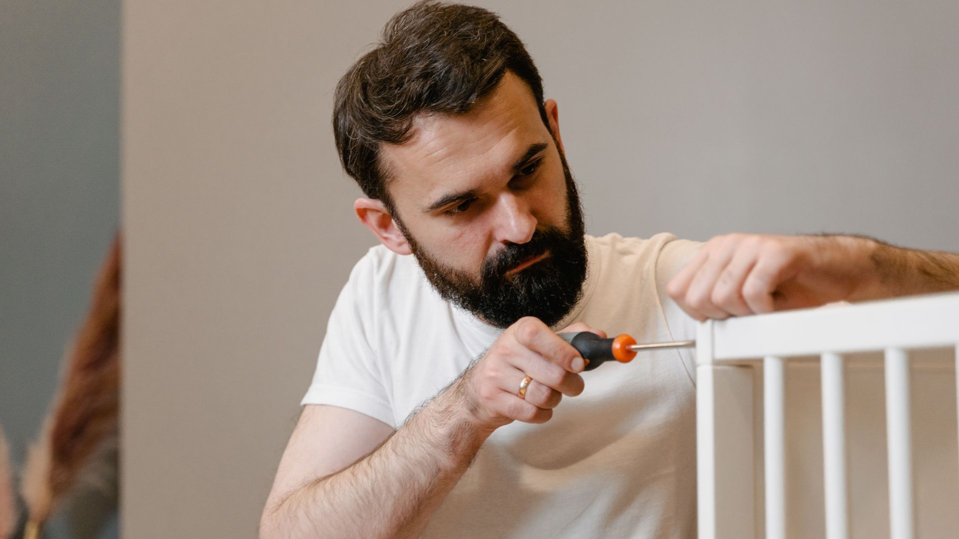 A man focusing closely on assembling a baby crib with a screwdriver in a well-lit room.
