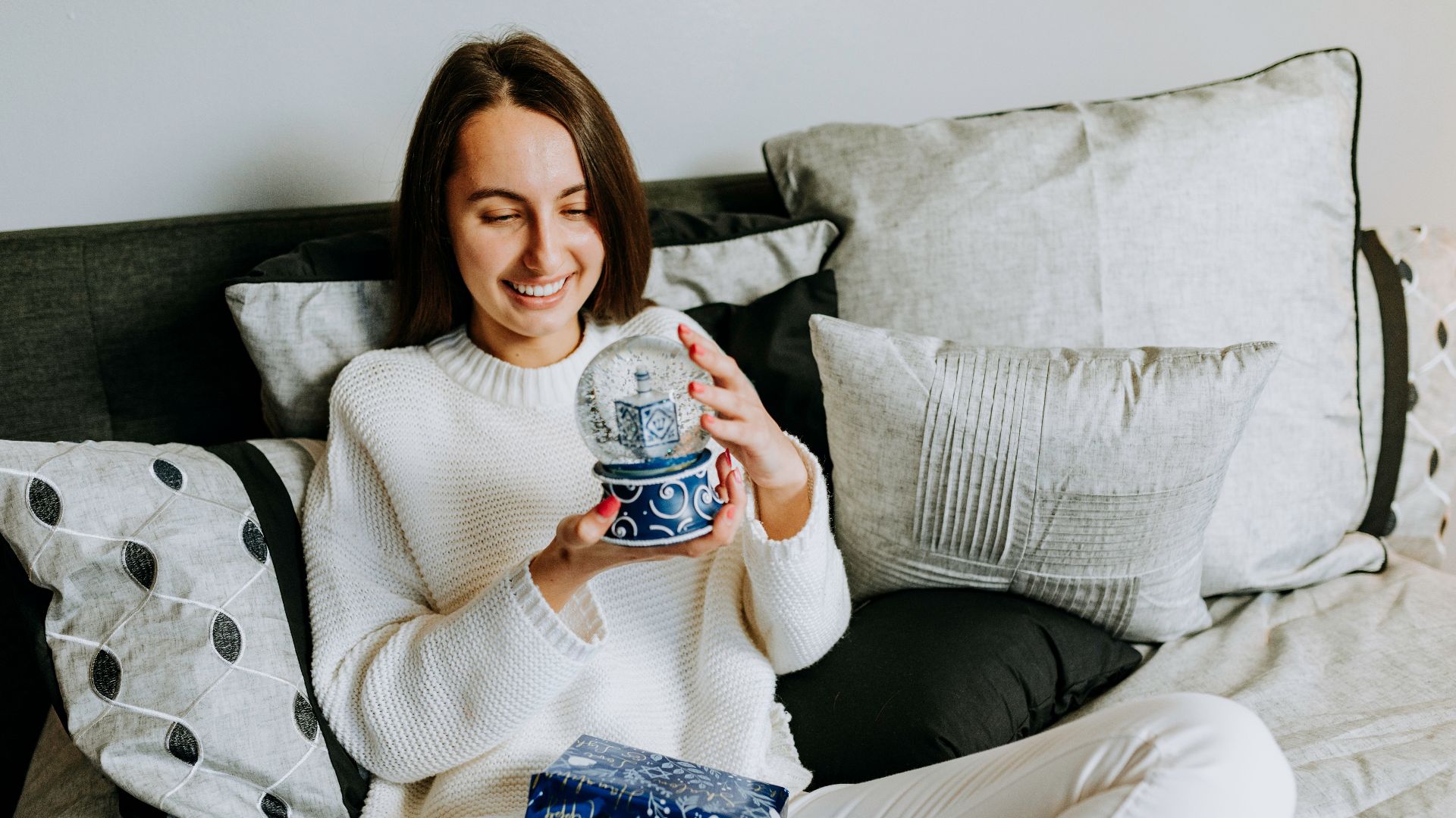 Smiling woman holding a Hanukkah-themed snow globe gift indoors.