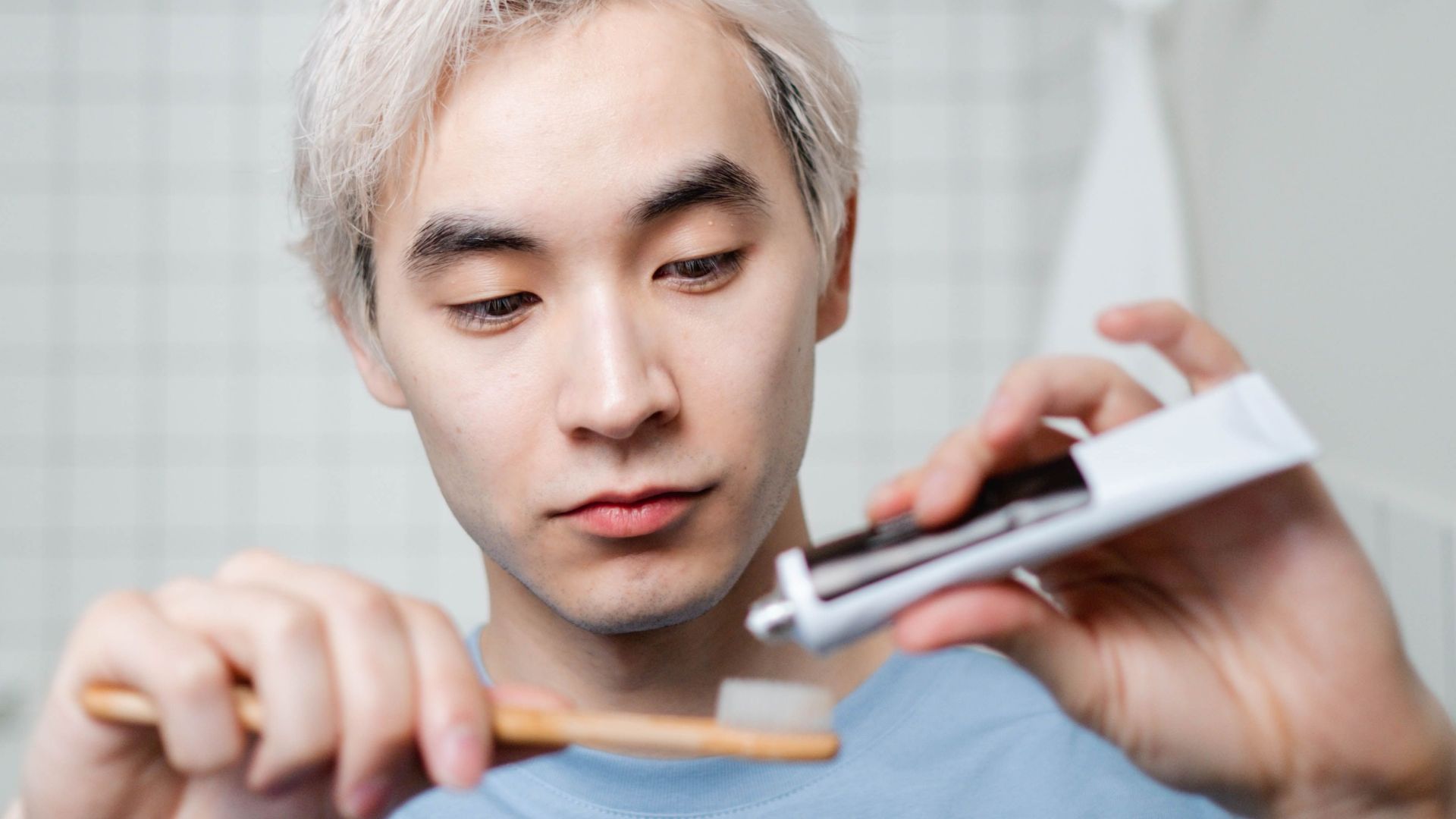 Young Asian man applying toothpaste to a brush during his morning oral hygiene routine.