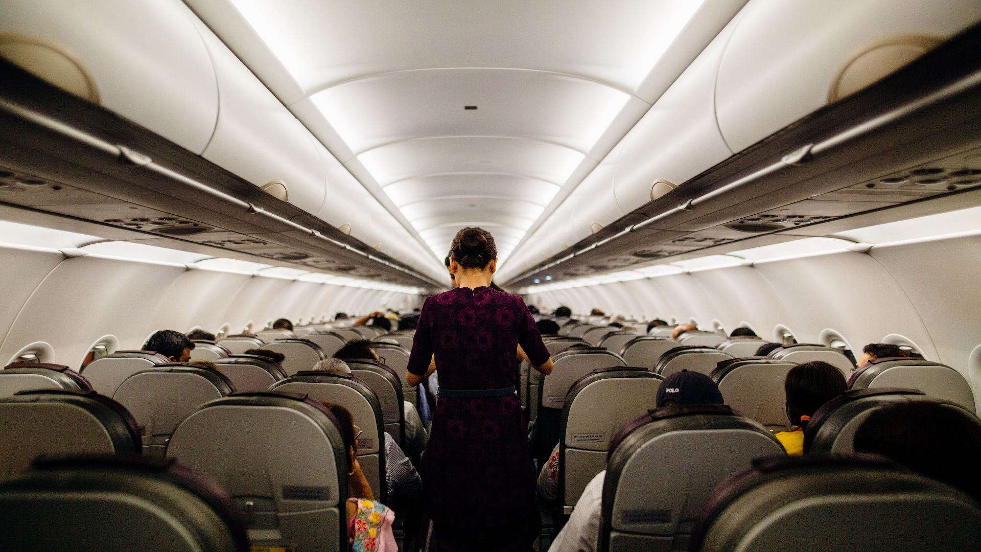 Interior view of an airplane cabin with passengers seated and a flight attendant walking down the aisle.