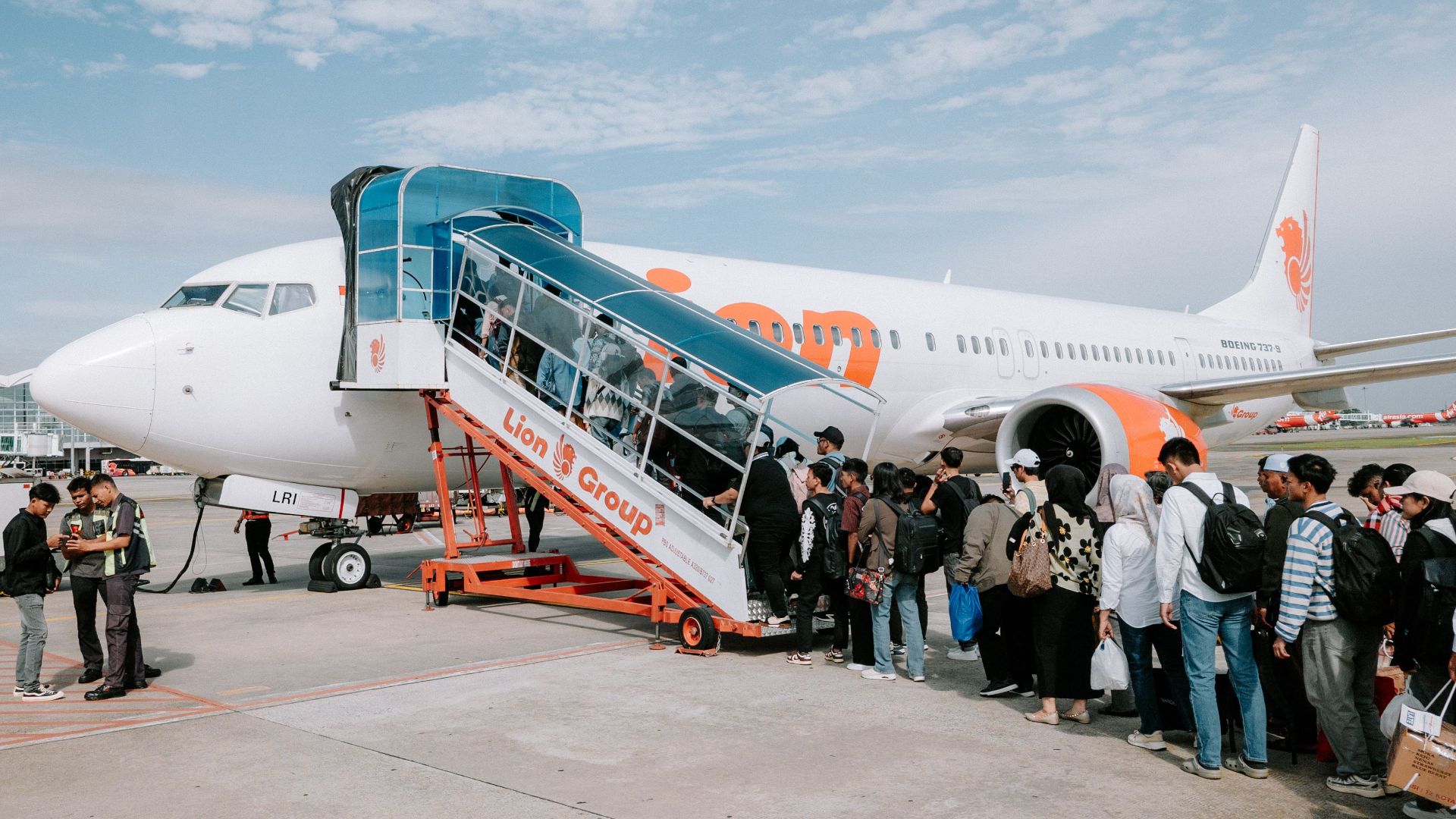 Travelers line up to board a Lion Air airplane at Medan Airport, Indonesia, during a sunny day.