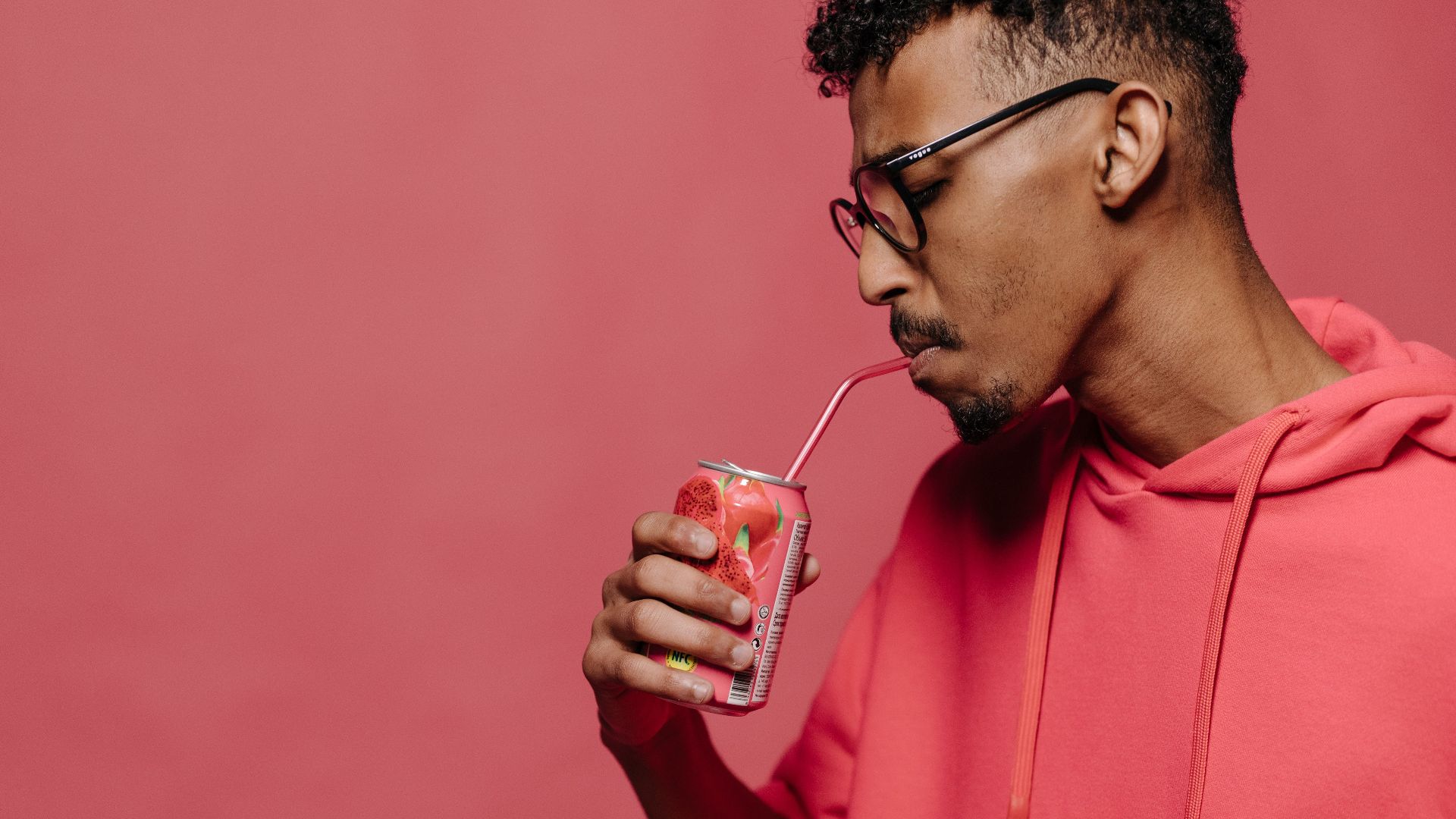 A stylish man drinks soda and holds a donut in a red themed studio setting.
