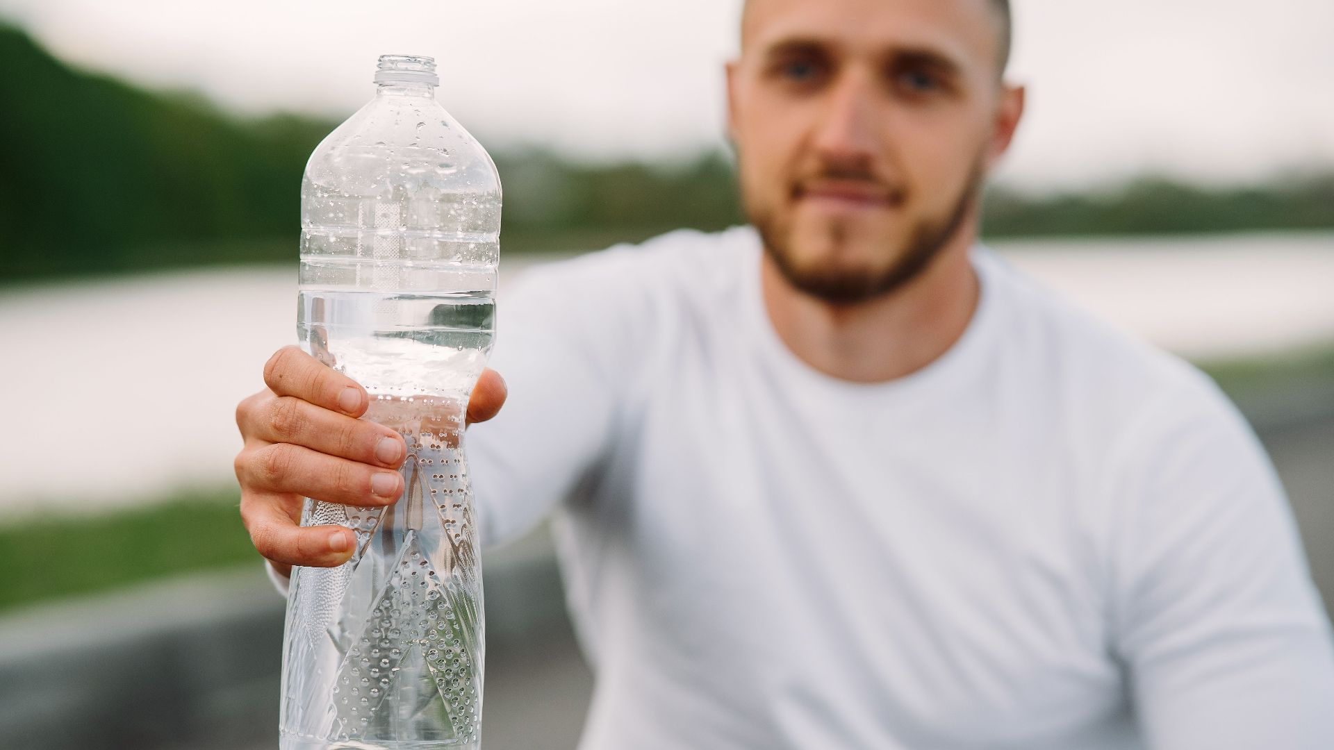 Man in sportswear offering a bottle of water outdoors, promoting hydration and fitness.