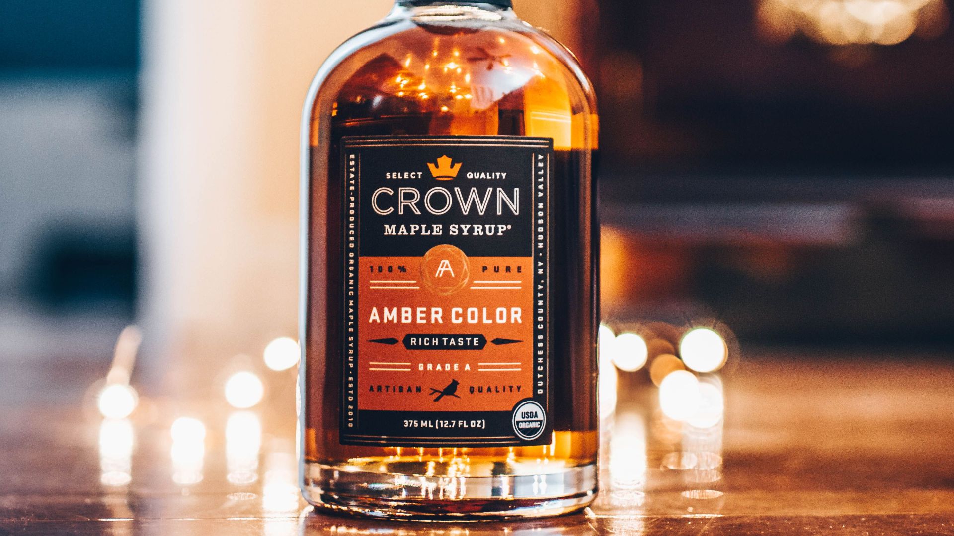 A close-up of a Crown maple syrup bottle showcasing rich amber color on a wooden surface.