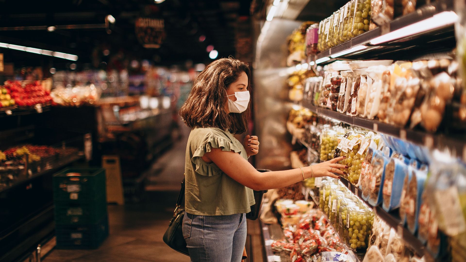 A woman wearing a mask shops for groceries in a supermarket aisle.