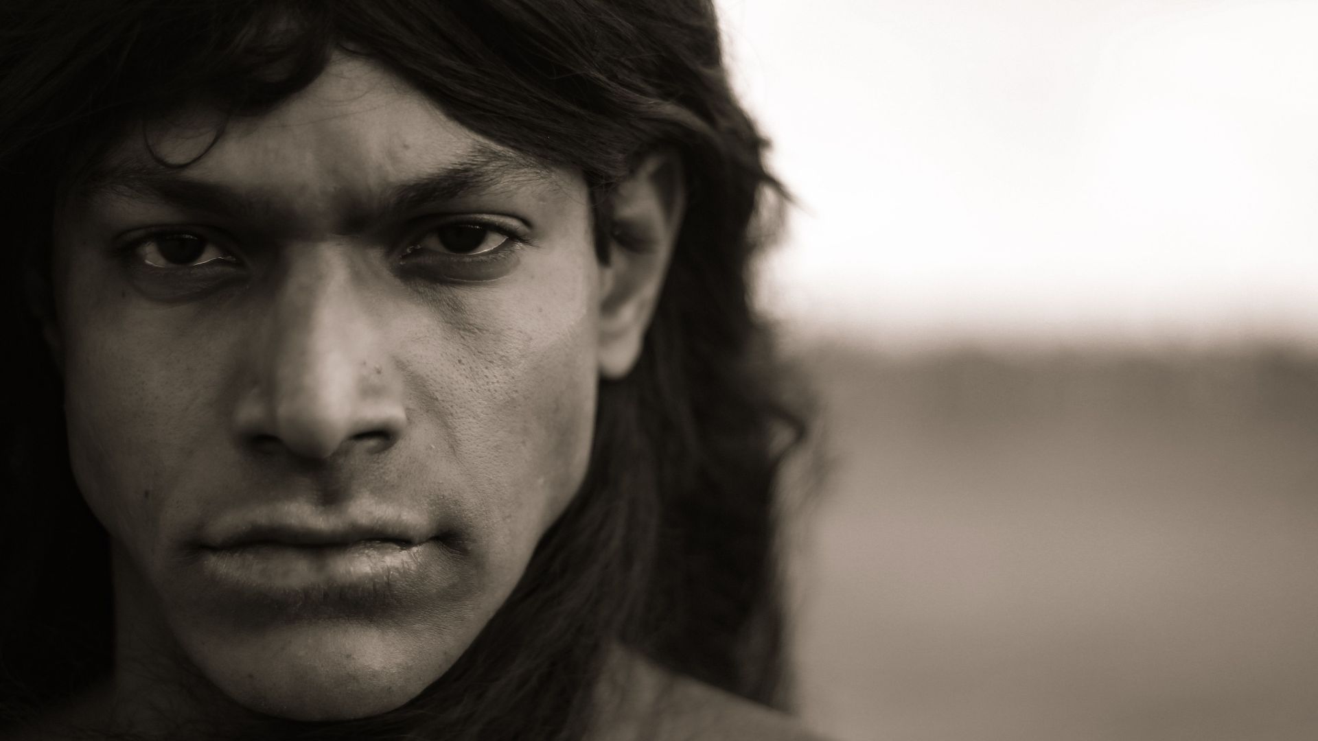Sepia-toned close-up portrait of a man with long hair, exuding a dramatic and intense mood.