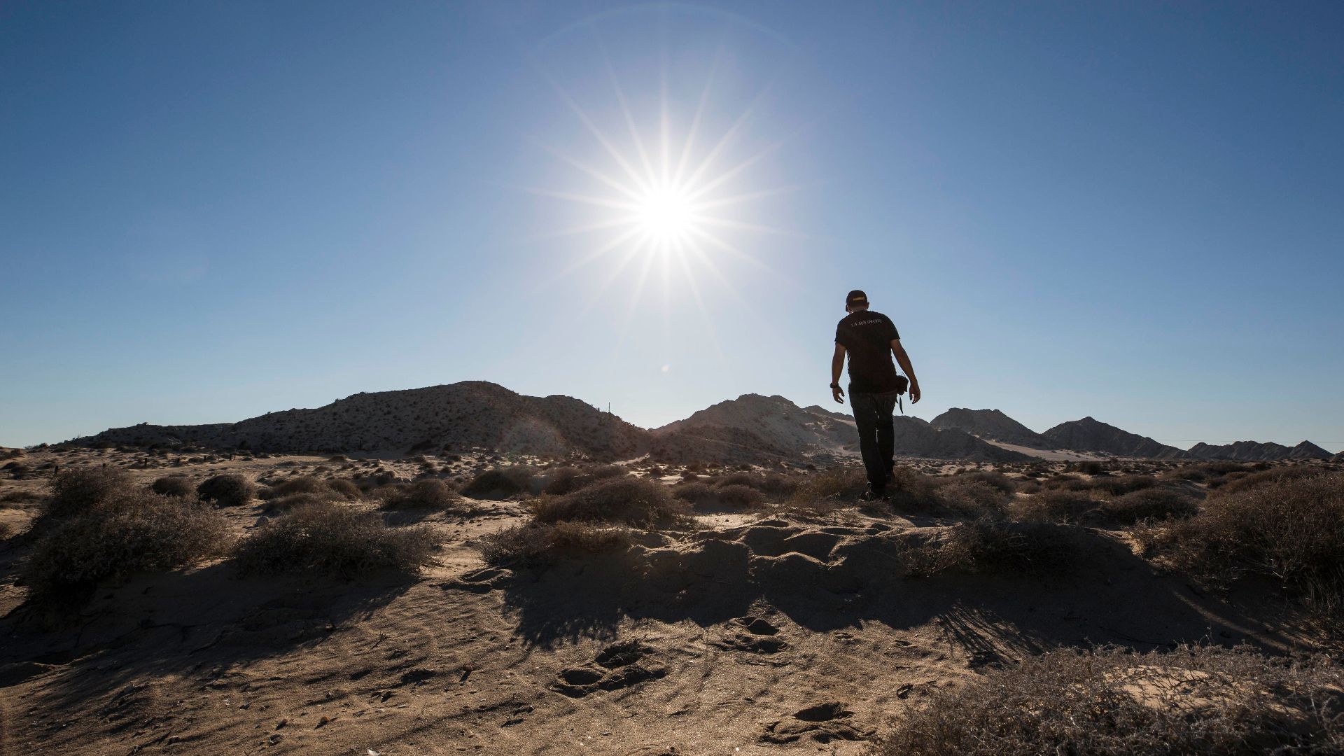 Man walking in Puerto Peñasco desert landscape under bright sun.