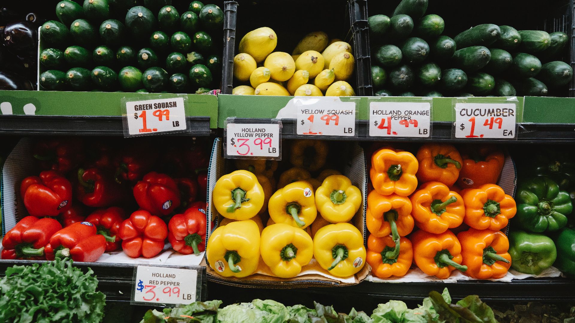 Colorful assortment of fresh vegetables at a supermarket display, highlighting peppers, squash, and cucumbers.
