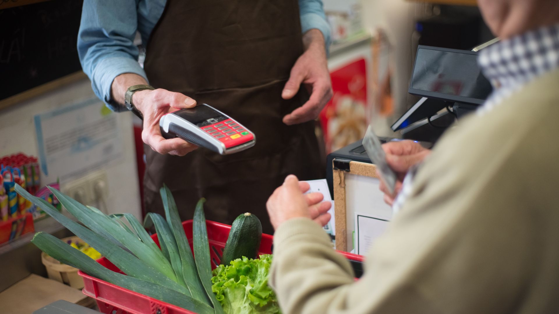 Close-up of customer paying for groceries with produce at a store checkout counter.