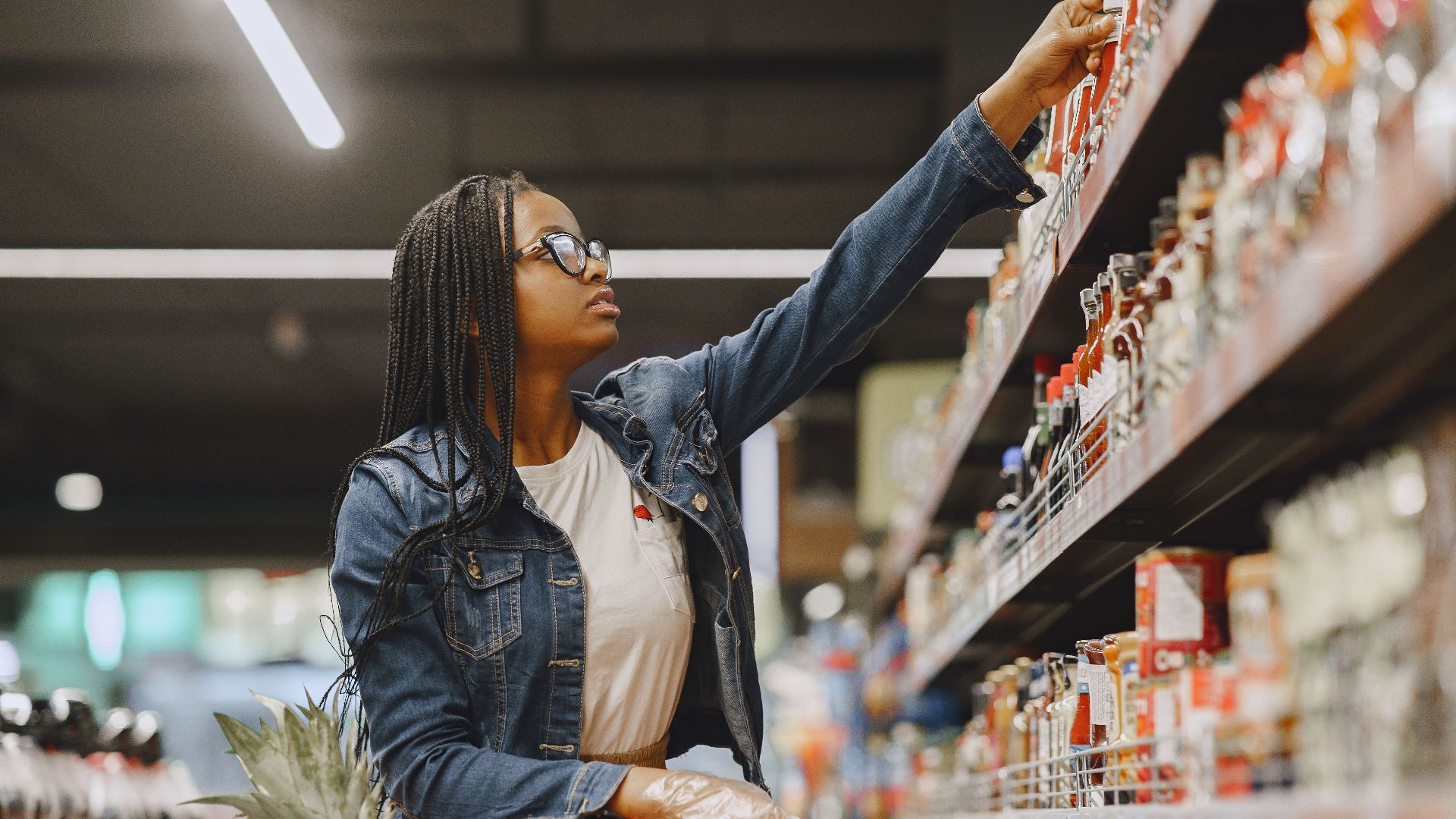 African American woman selecting items in a grocery store aisle with a shopping cart.
