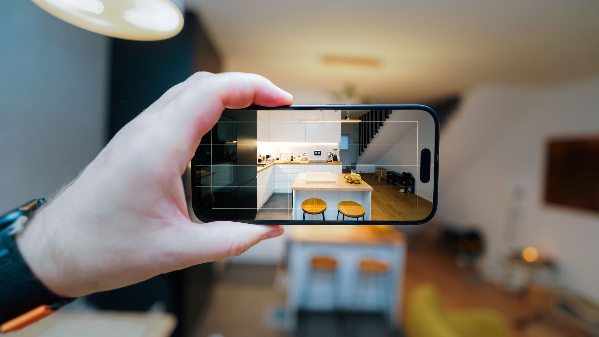A smartphone in focus capturing a modern kitchen interior, showcasing real estate potential.