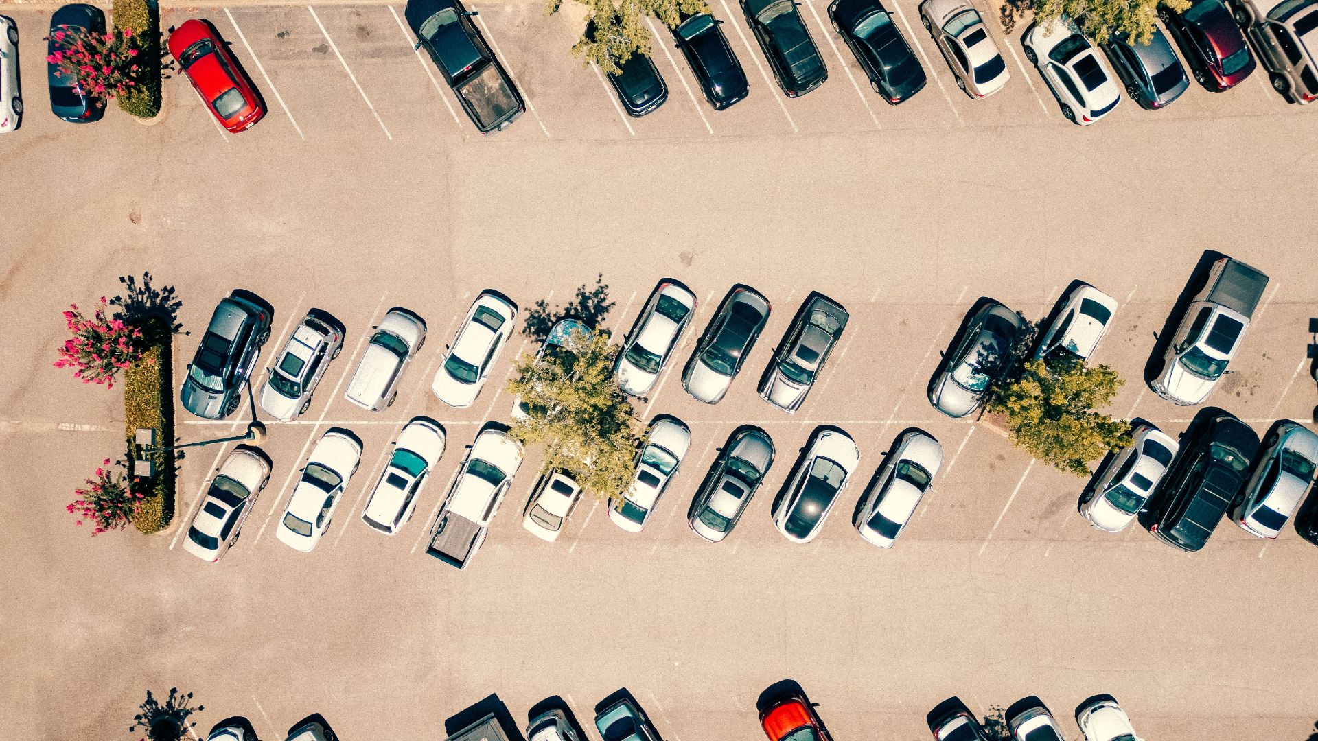 Aerial shot of a parking lot filled with cars on a bright, sunny day.