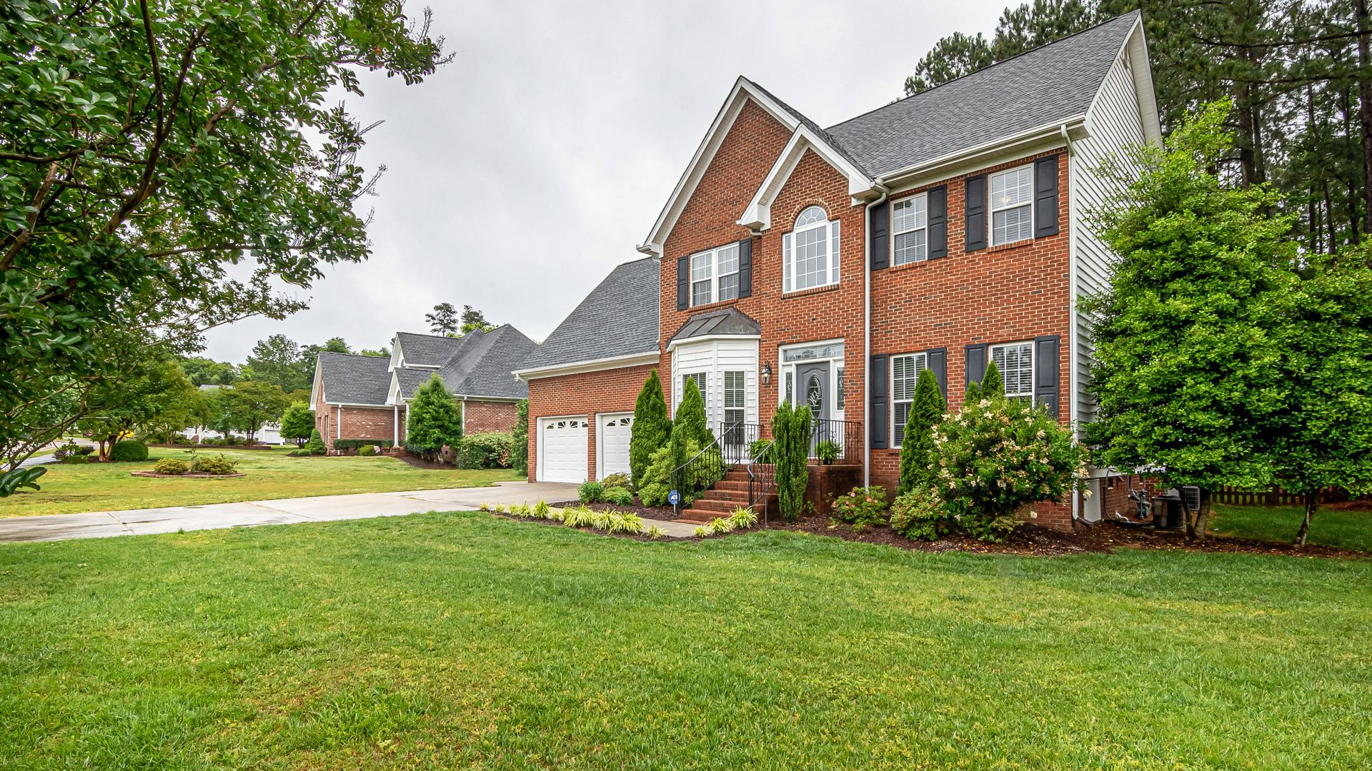 Charming two-story brick house with manicured lawn and trees, perfect family home.