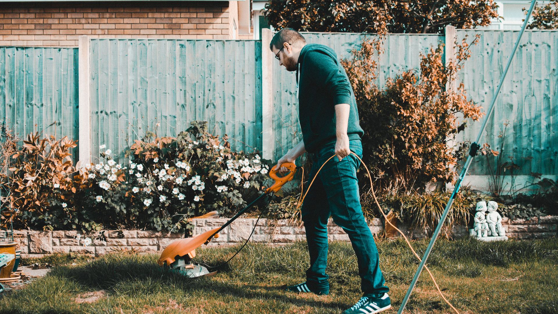 A man using an electric mower in a garden on a sunny day, capturing outdoor chores and gardening vibes.