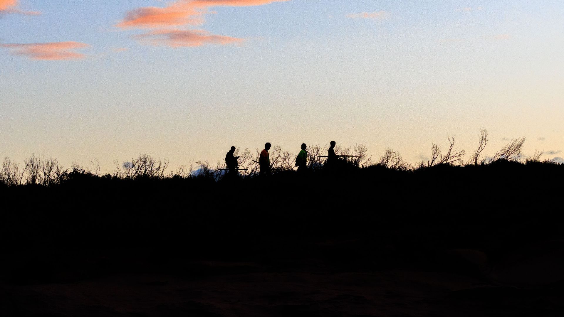 A group of people walking along a ridge at sunset, silhouetted against a serene sky.