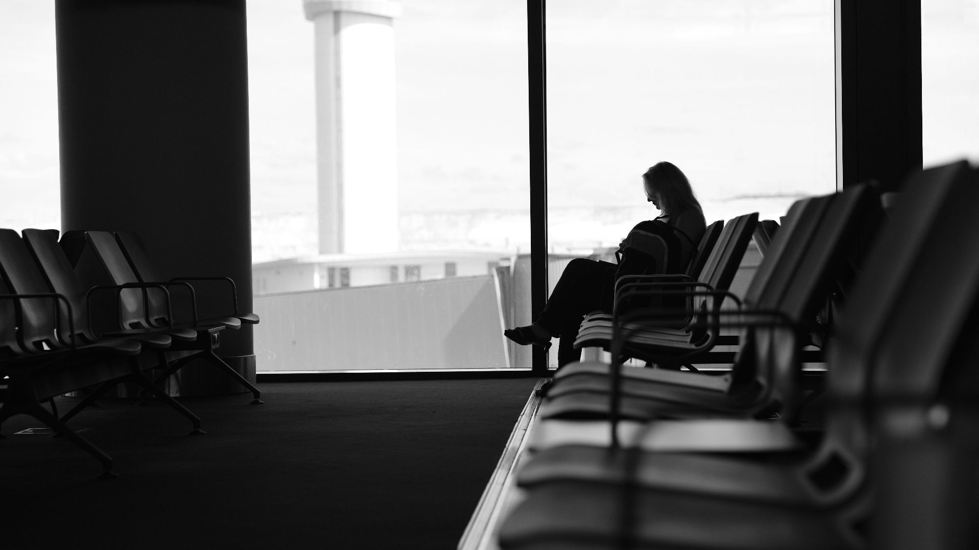 Silhouette of a woman sitting in an airport terminal lounge, with view of control tower.